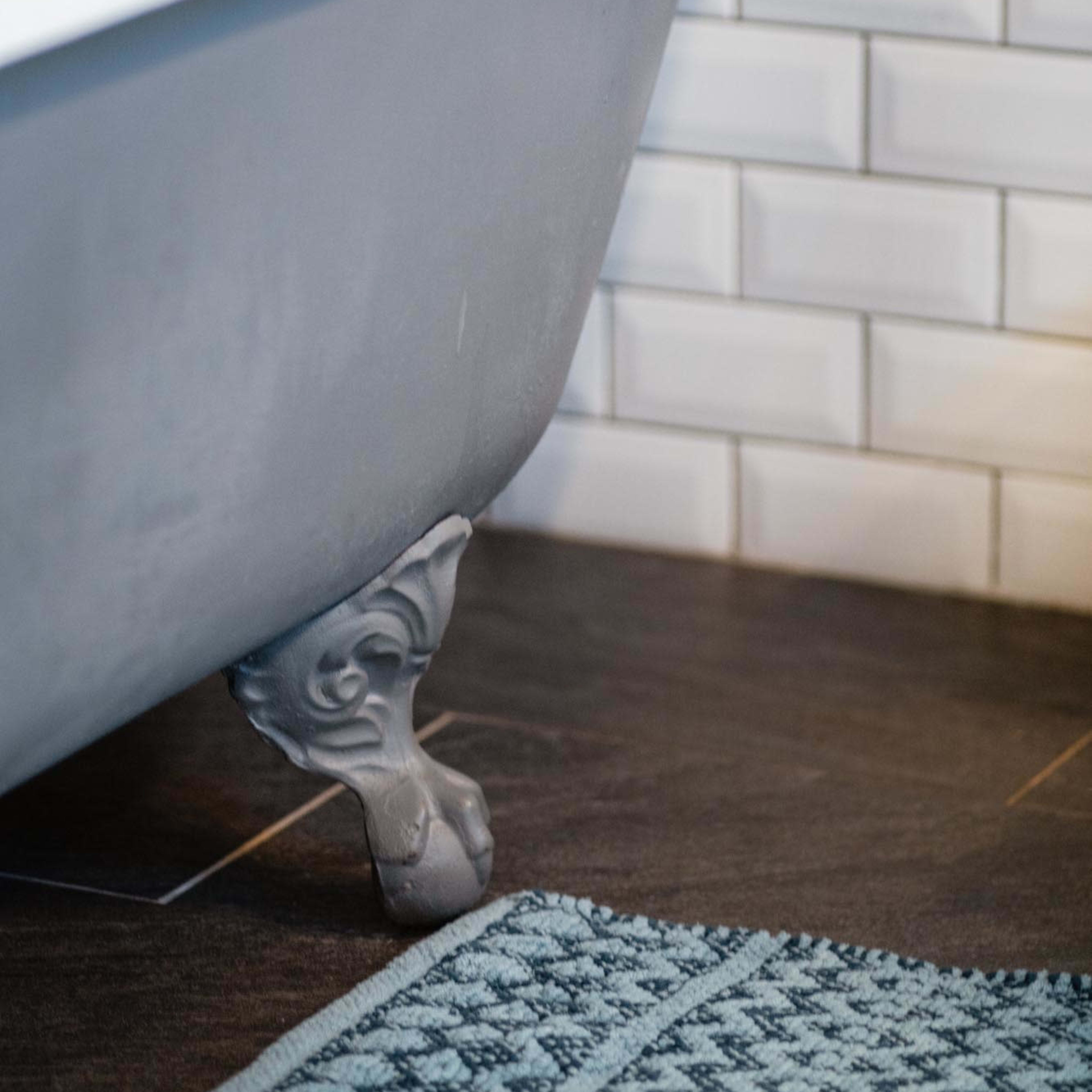 A vintage clawfoot bathtub with a white rim sits near a tiled wall and a textured blue bath mat on the floor.