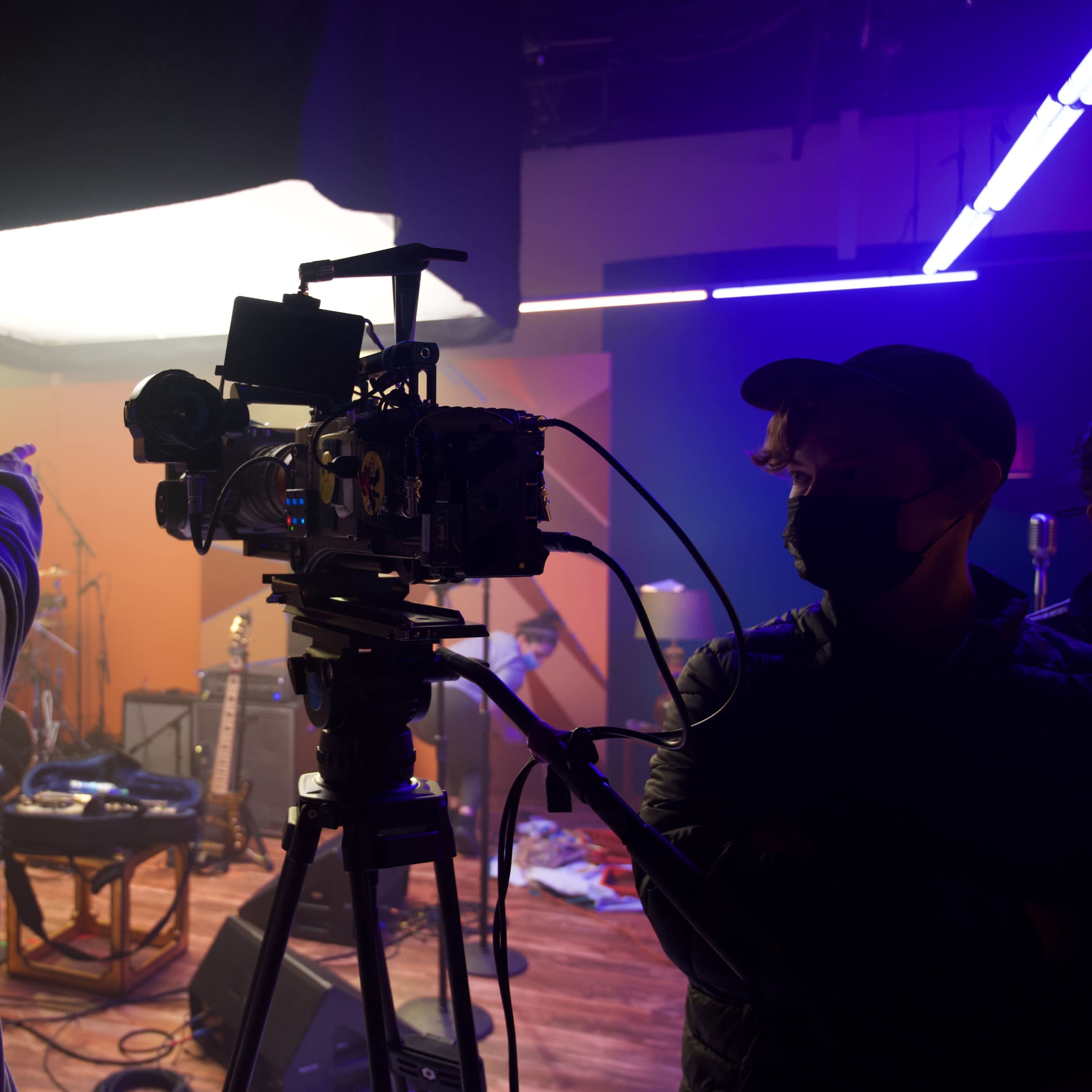 A film crew sets up equipment in a studio, with one crew member pointing while another operates a camera.