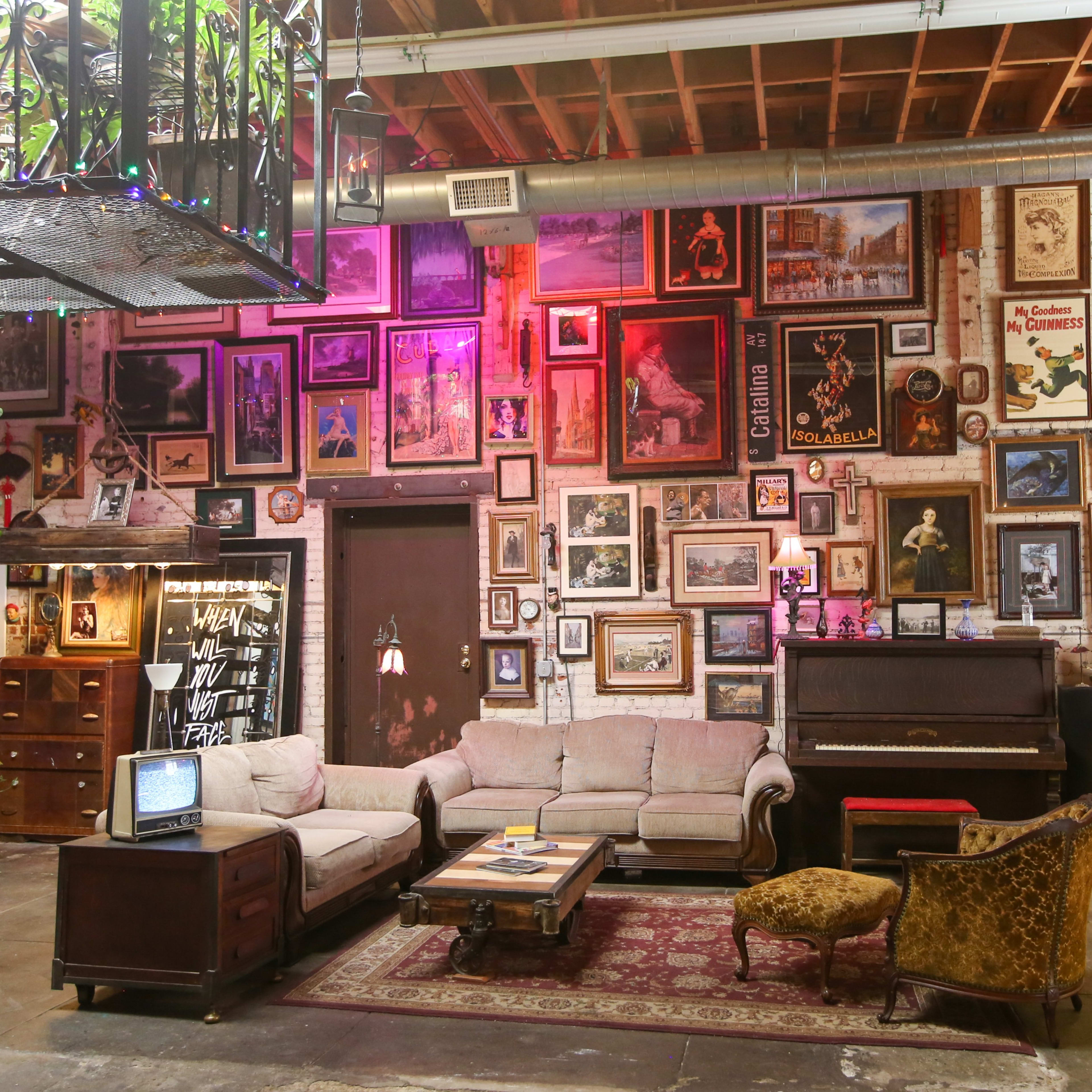 A vintage-style lounge area featuring a sofa, armchair, a piano, and walls adorned with an eclectic collection of framed artwork and photographs.
