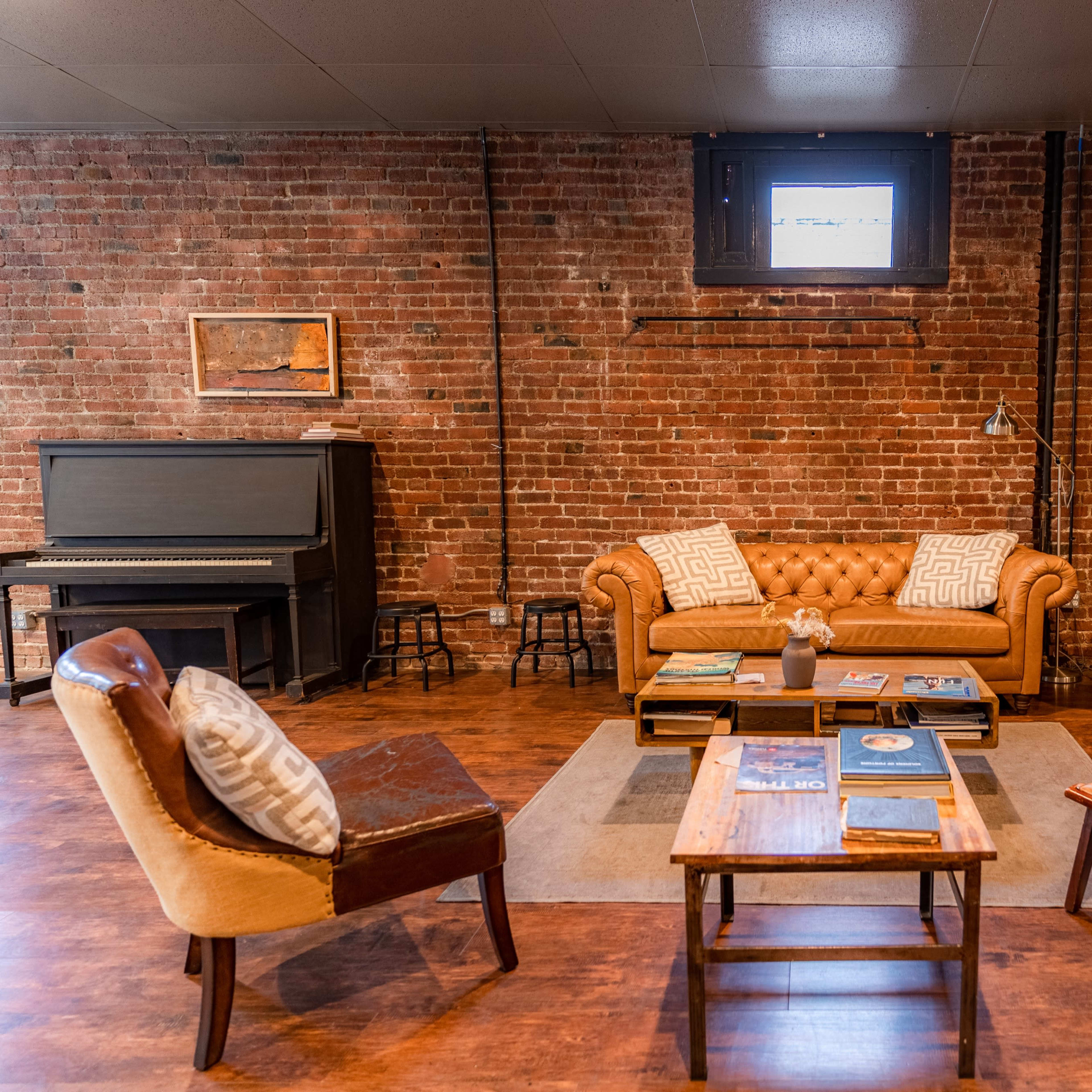 A cozy lounge area with a leather sofa, a wooden coffee table, and various seating options, against a backdrop of exposed brick walls.