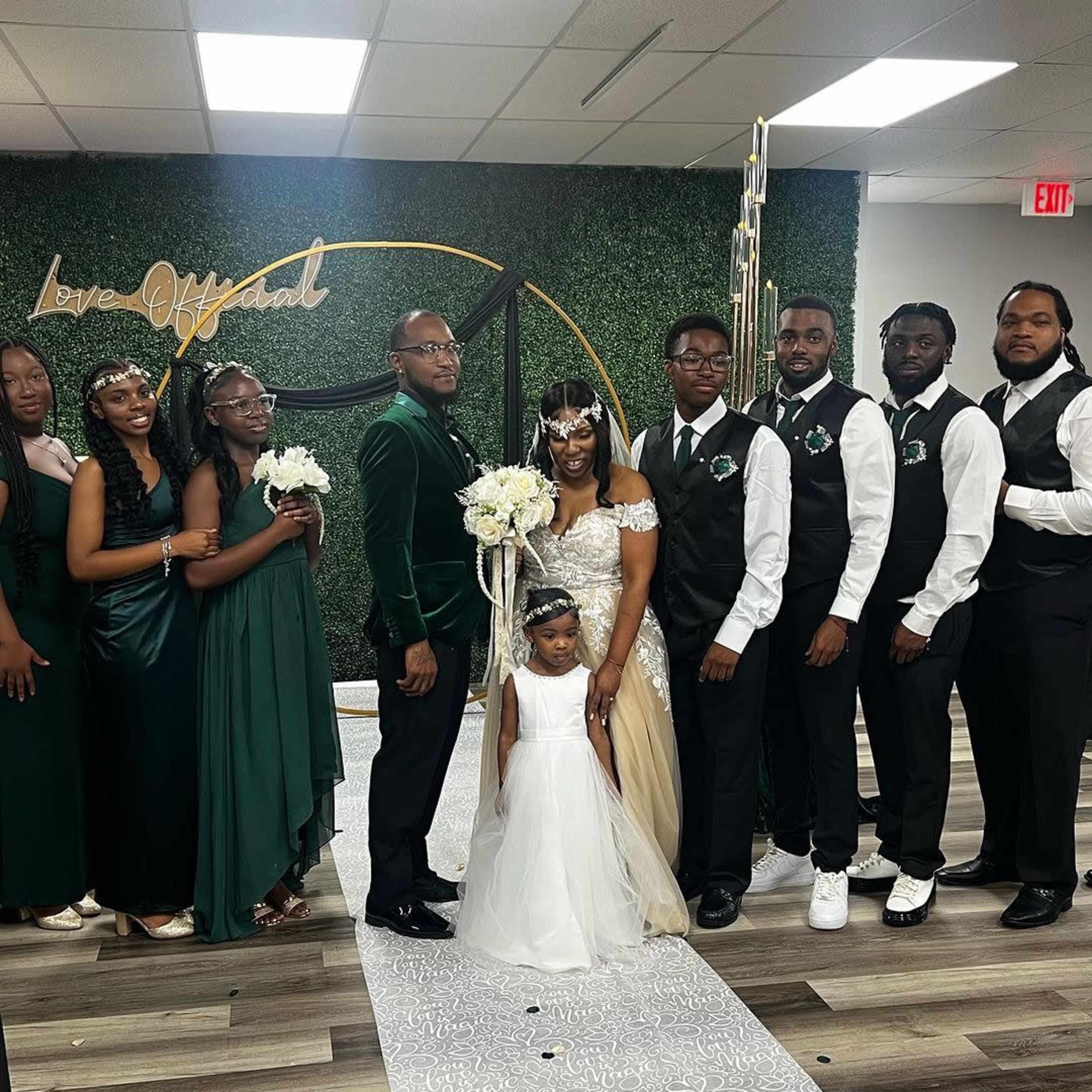 A wedding party poses together in a decorated venue with greenery and elegant decor.