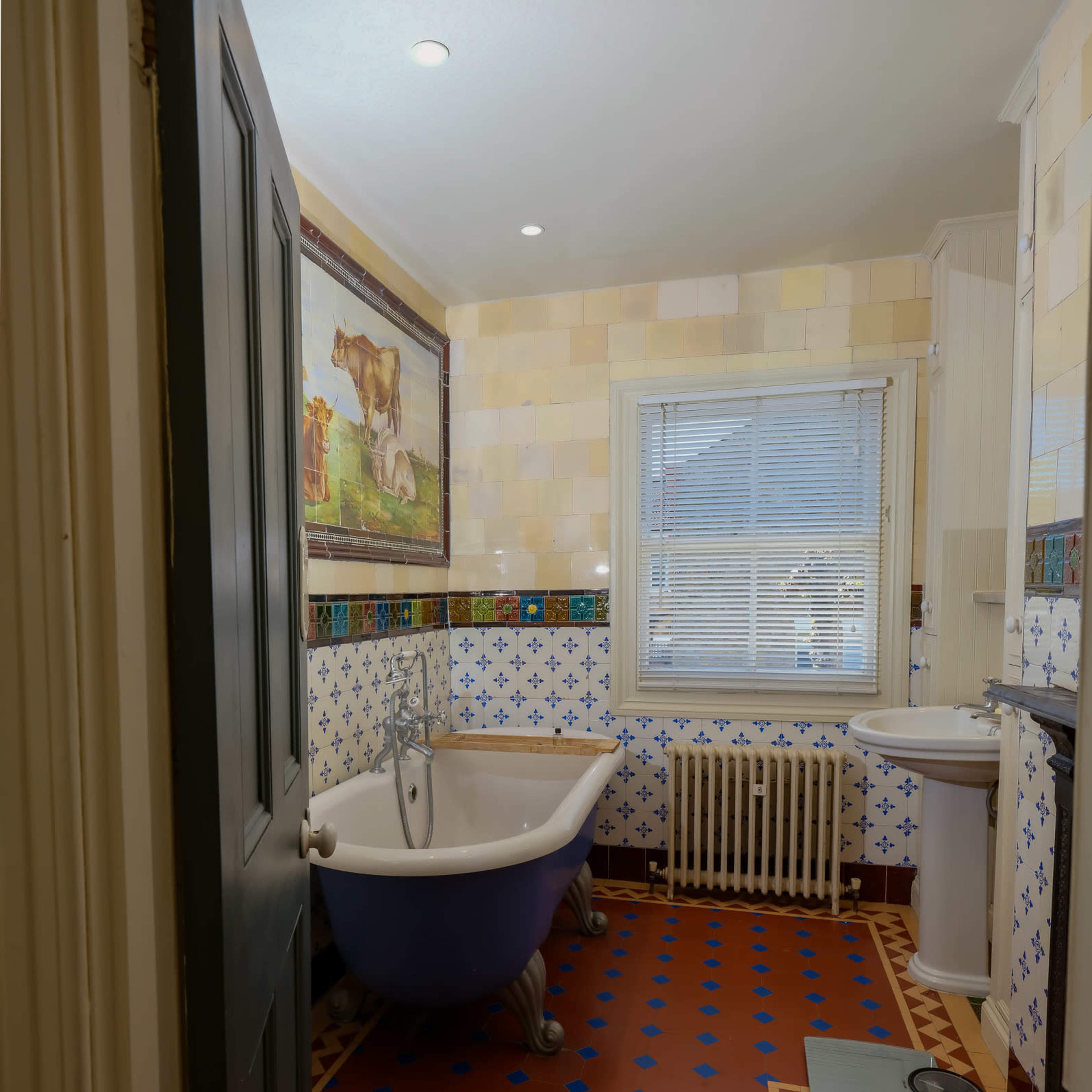 A bathroom featuring a clawfoot bathtub, a pedestal sink, a radiator, and tiled walls with a decorative border.