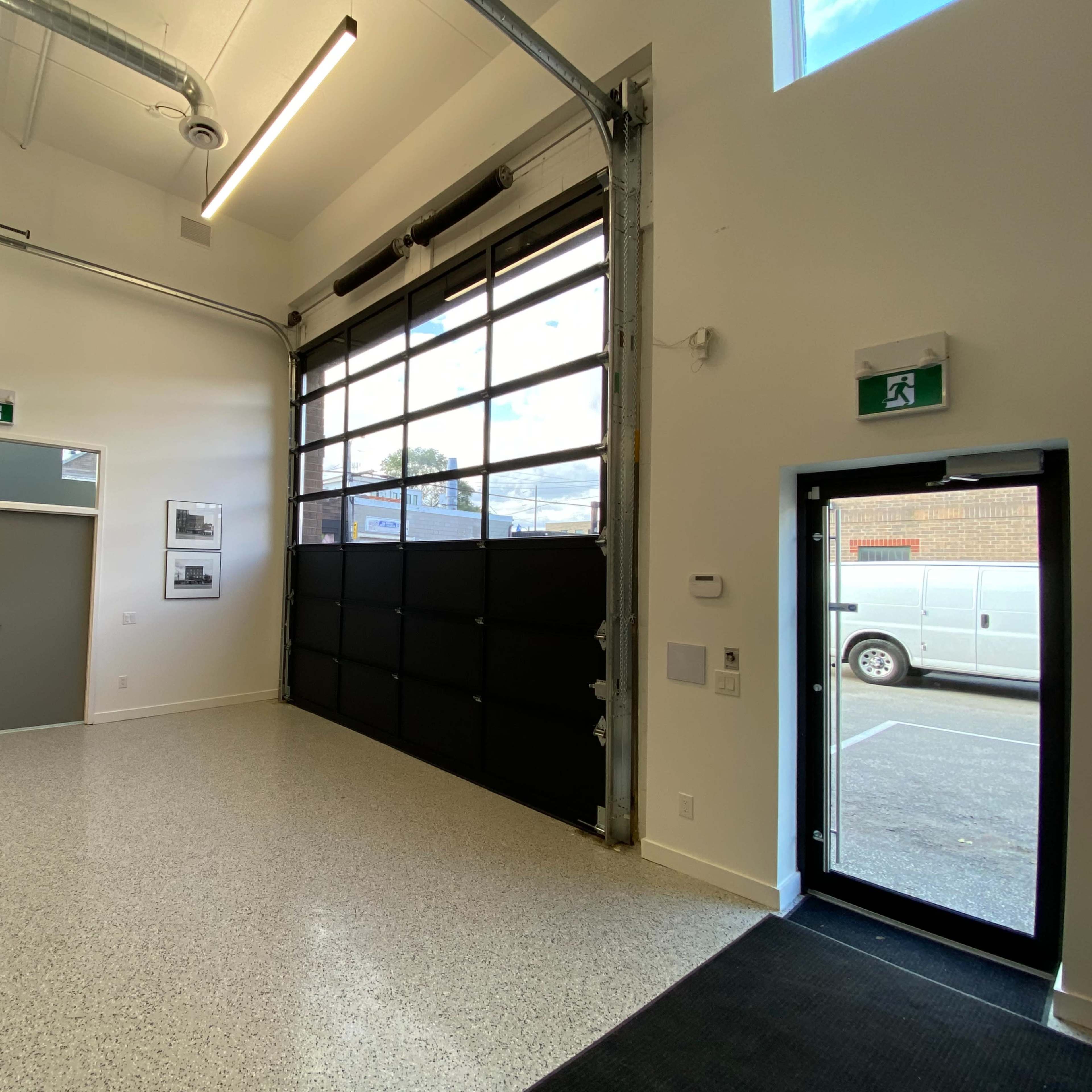 An indoor space with a large glass garage door, two doors on the left side, a small table with wooden top and metal legs, and a view of a parked vehicle outside.