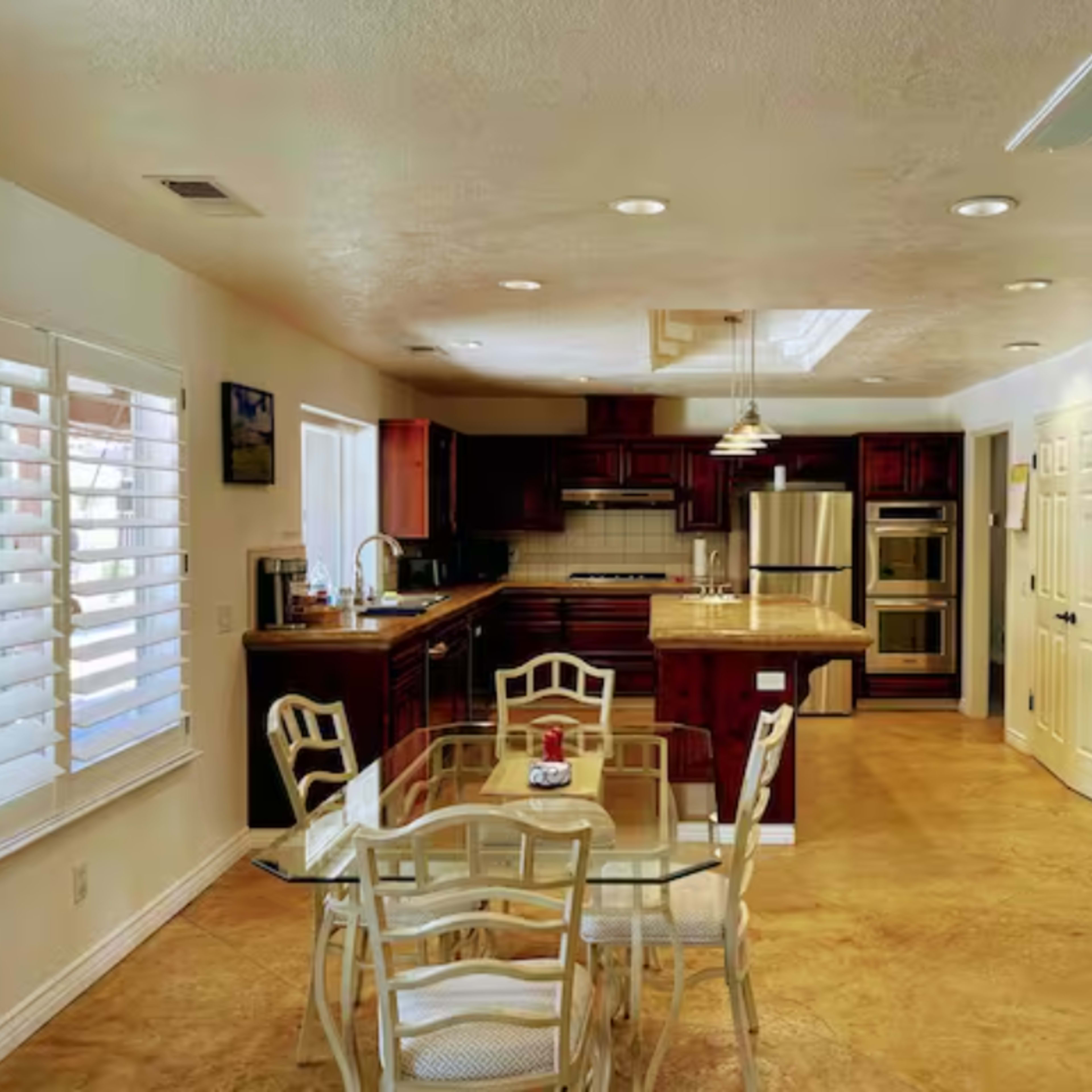 A spacious kitchen with wooden cabinetry, stainless steel appliances, and a dining area featuring a glass table and chairs.