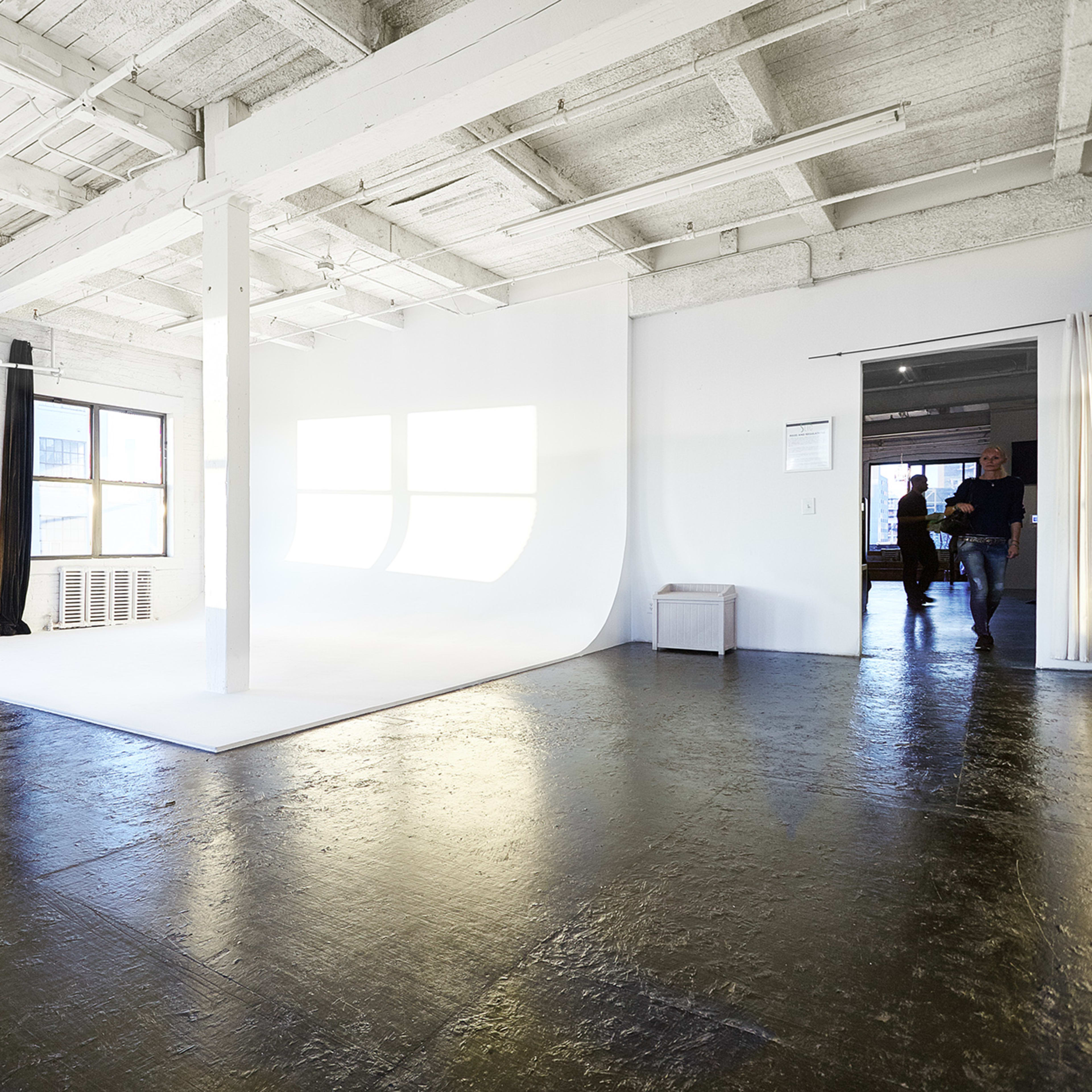 A spacious studio with white walls, large windows, and a seamless backdrop.