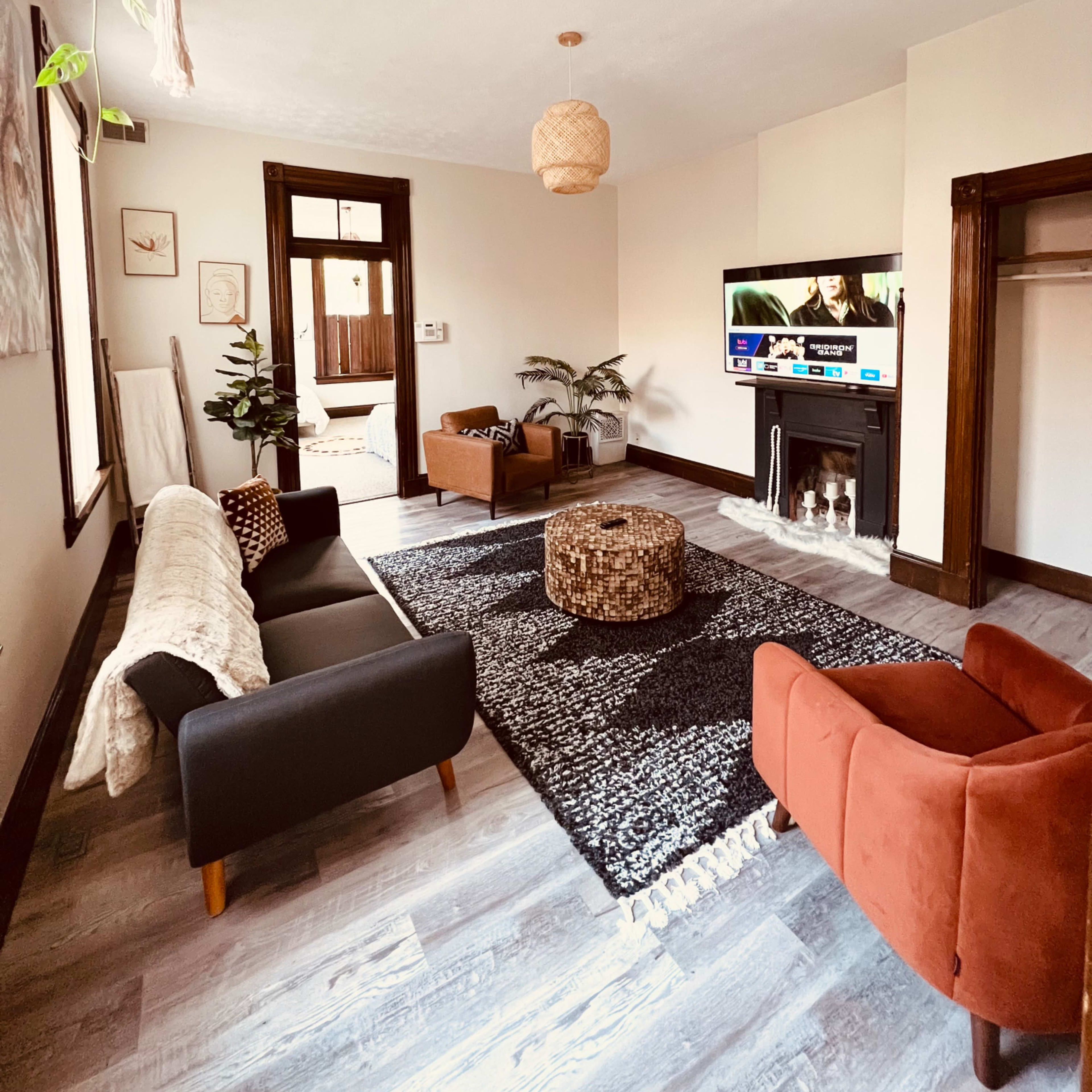 A living room with two armchairs, a sofa, a coffee table, a television, and decorative plants on wooden floors.