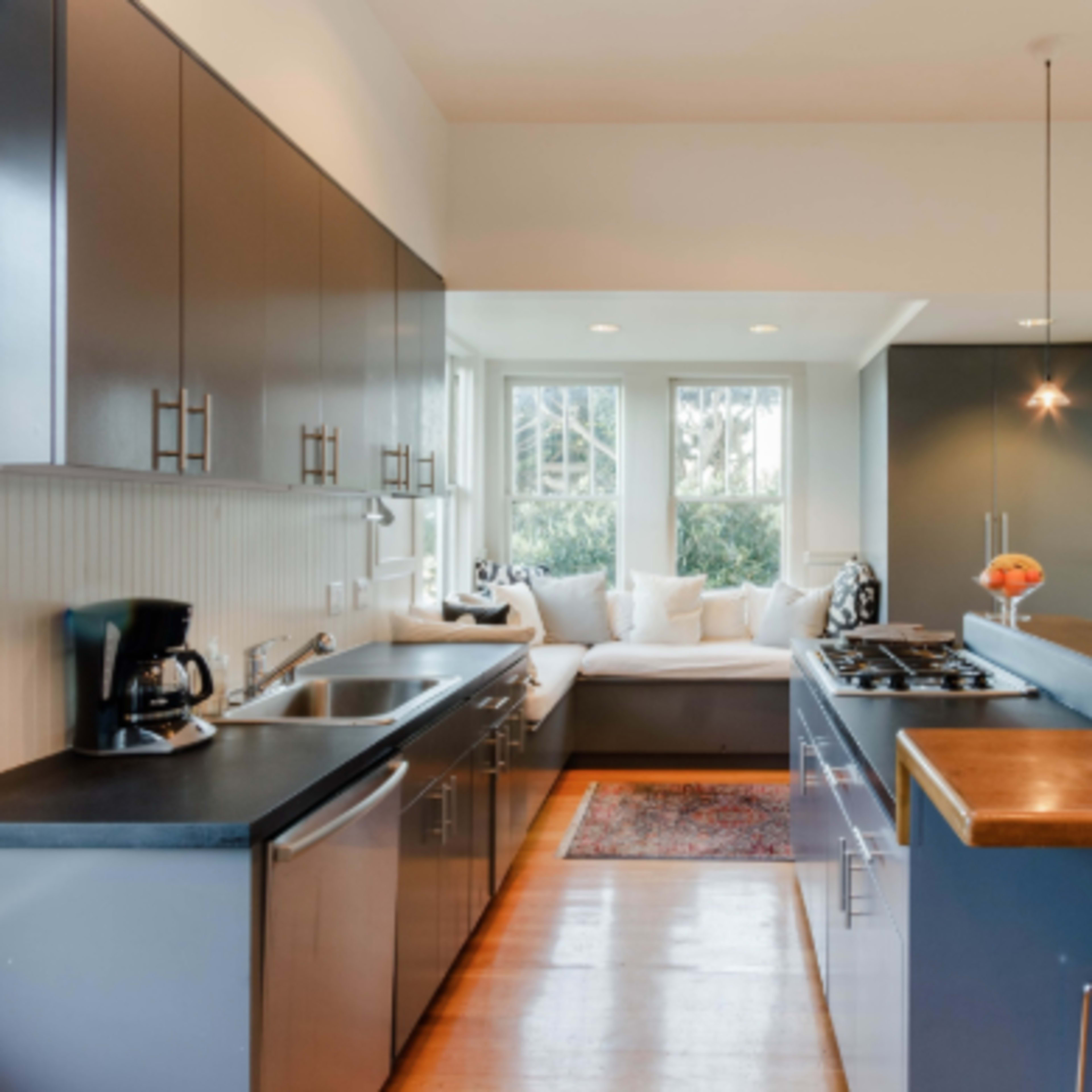 A modern kitchen features dark cabinetry, stainless steel appliances, and a dining bar with stools, illuminated by pendant lights.