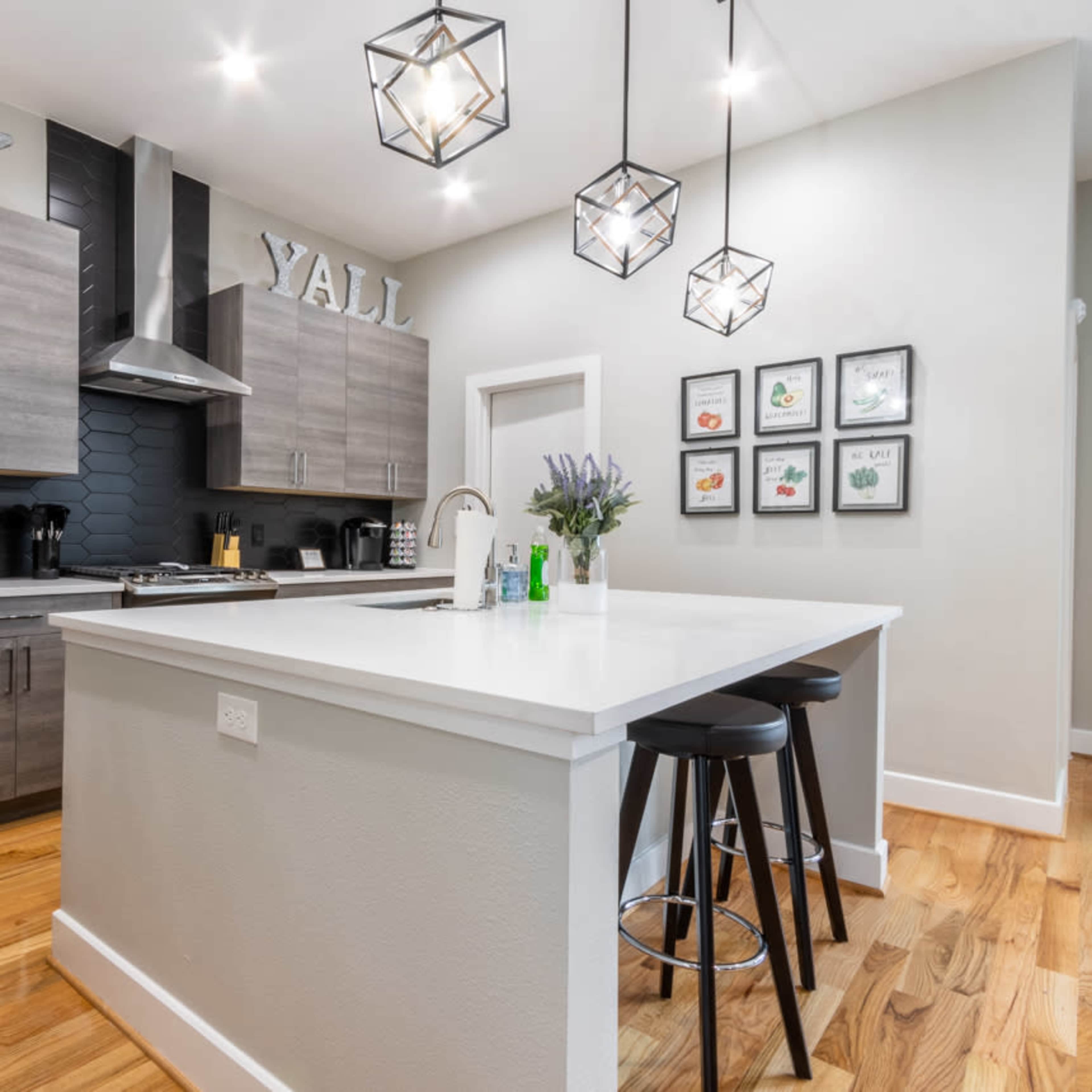 A modern kitchen features gray cabinetry, a large island with bar stools, and decorative lighting.