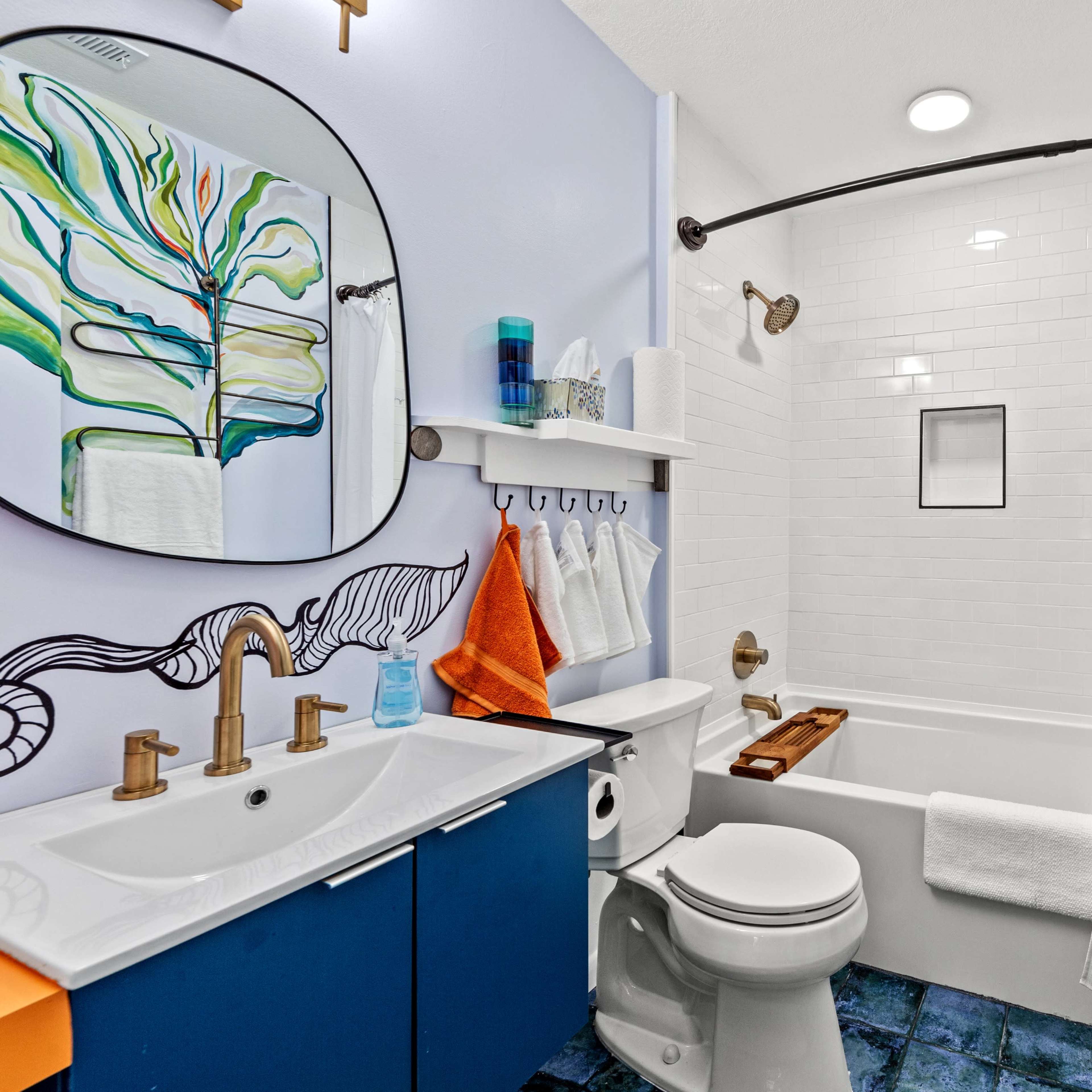 A modern bathroom featuring a bathtub with a shower curtain, a circular mirror above a double sink, and colorful wall decorations.