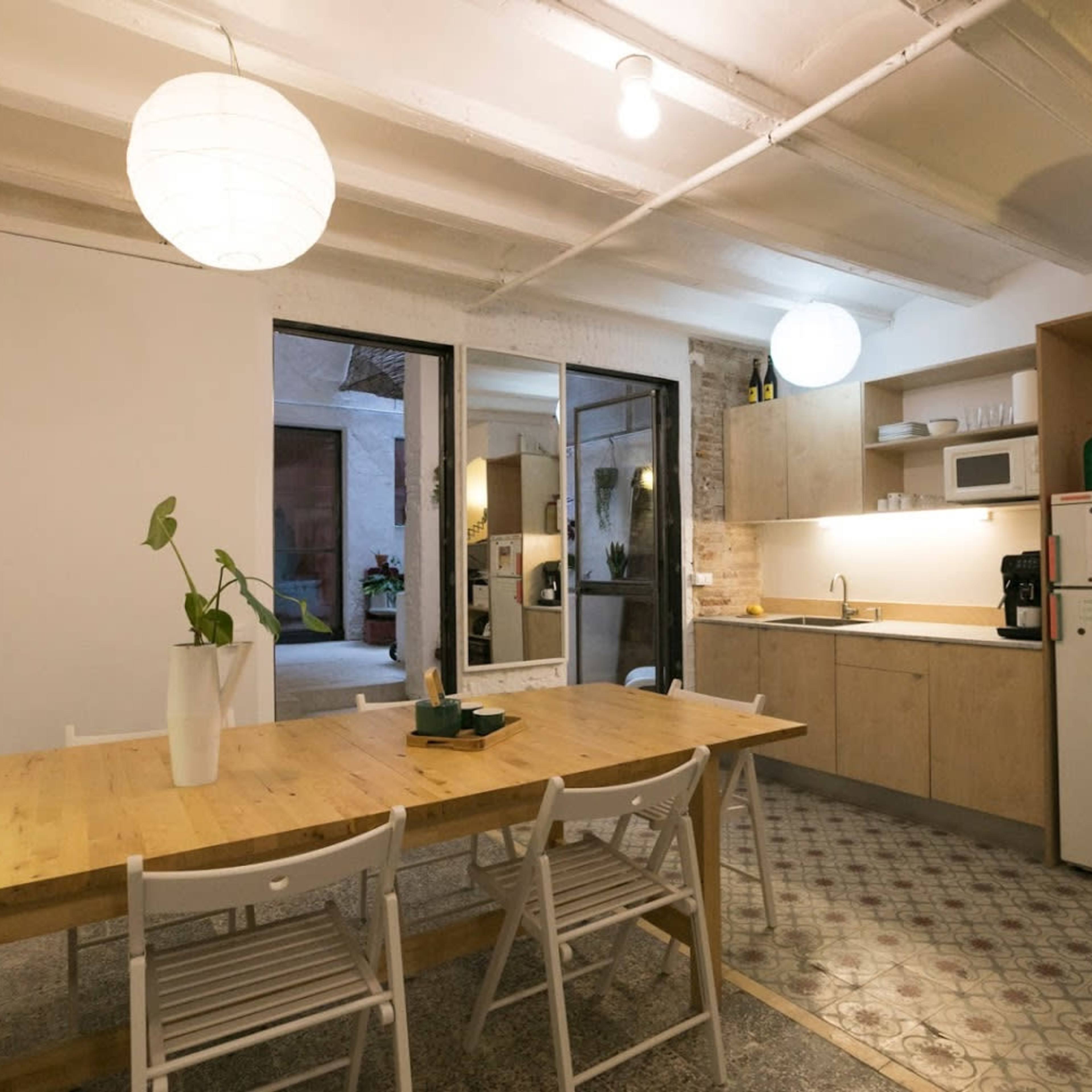 A spacious kitchen and dining area features a wooden table, minimalist decor, and large windows that allow natural light to fill the space.