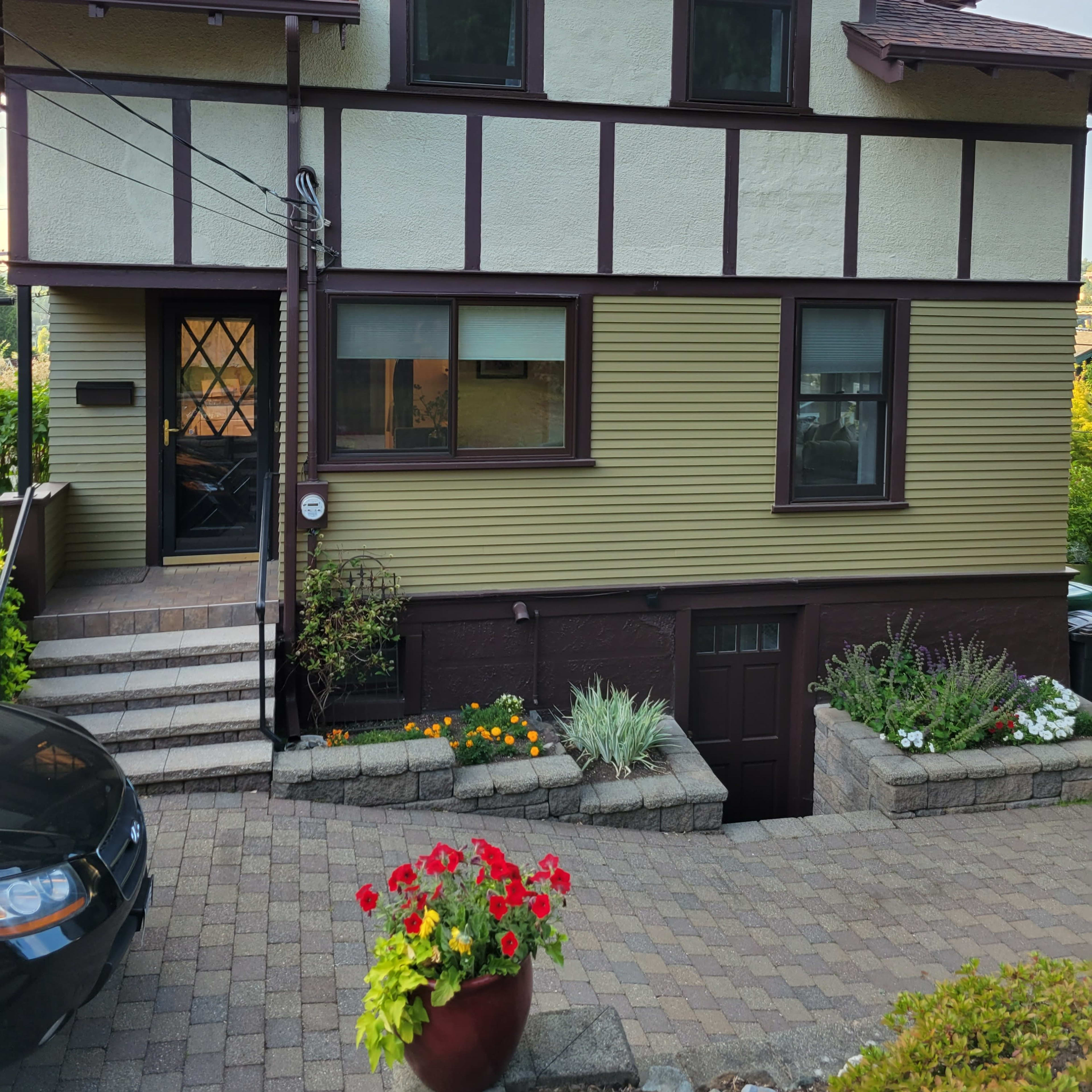 A two-story house with a combination of yellow and brown exterior, featuring a front entrance with steps and landscaped flower beds.