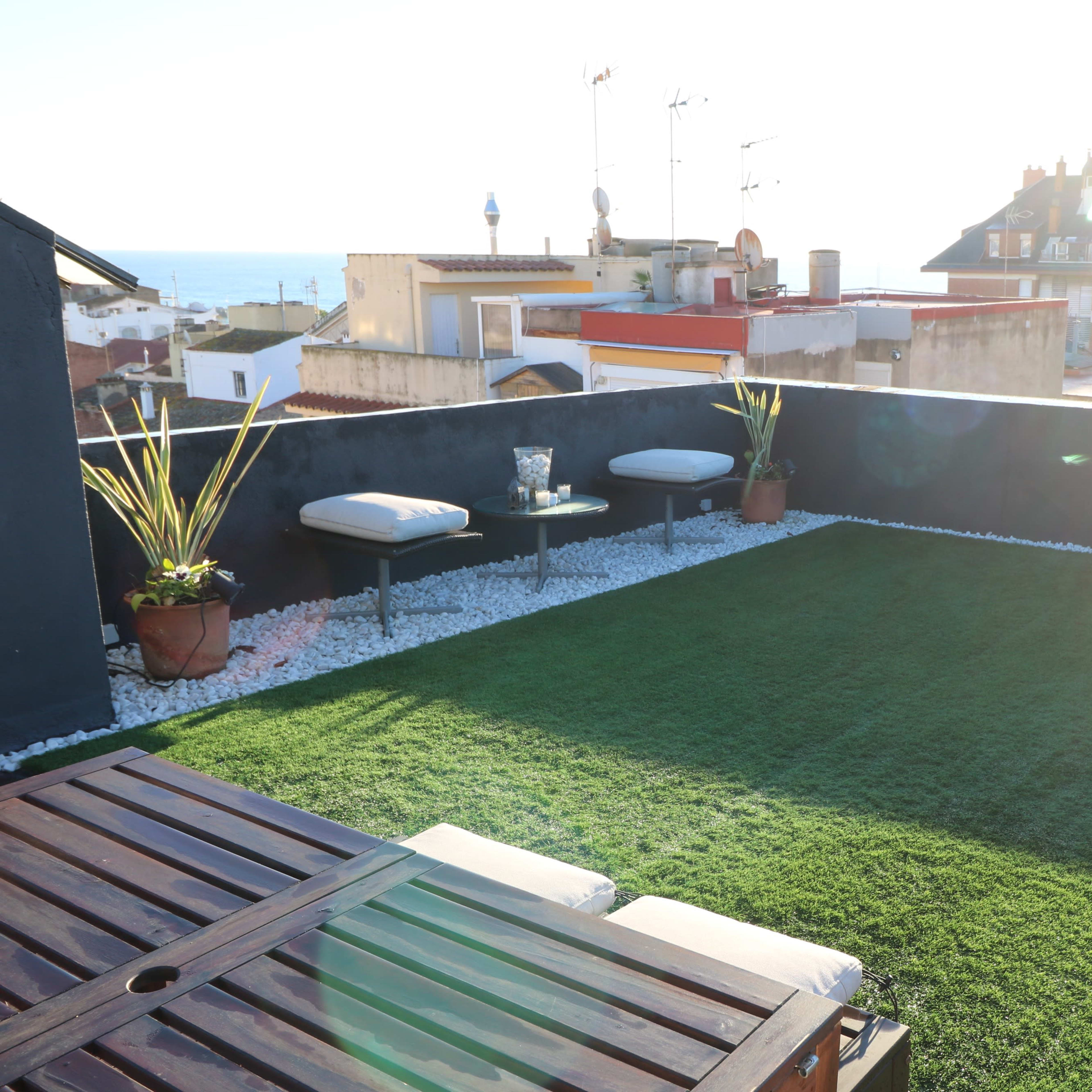 A rooftop terrace features artificial grass, a wooden table, lounge chairs, and sea views.