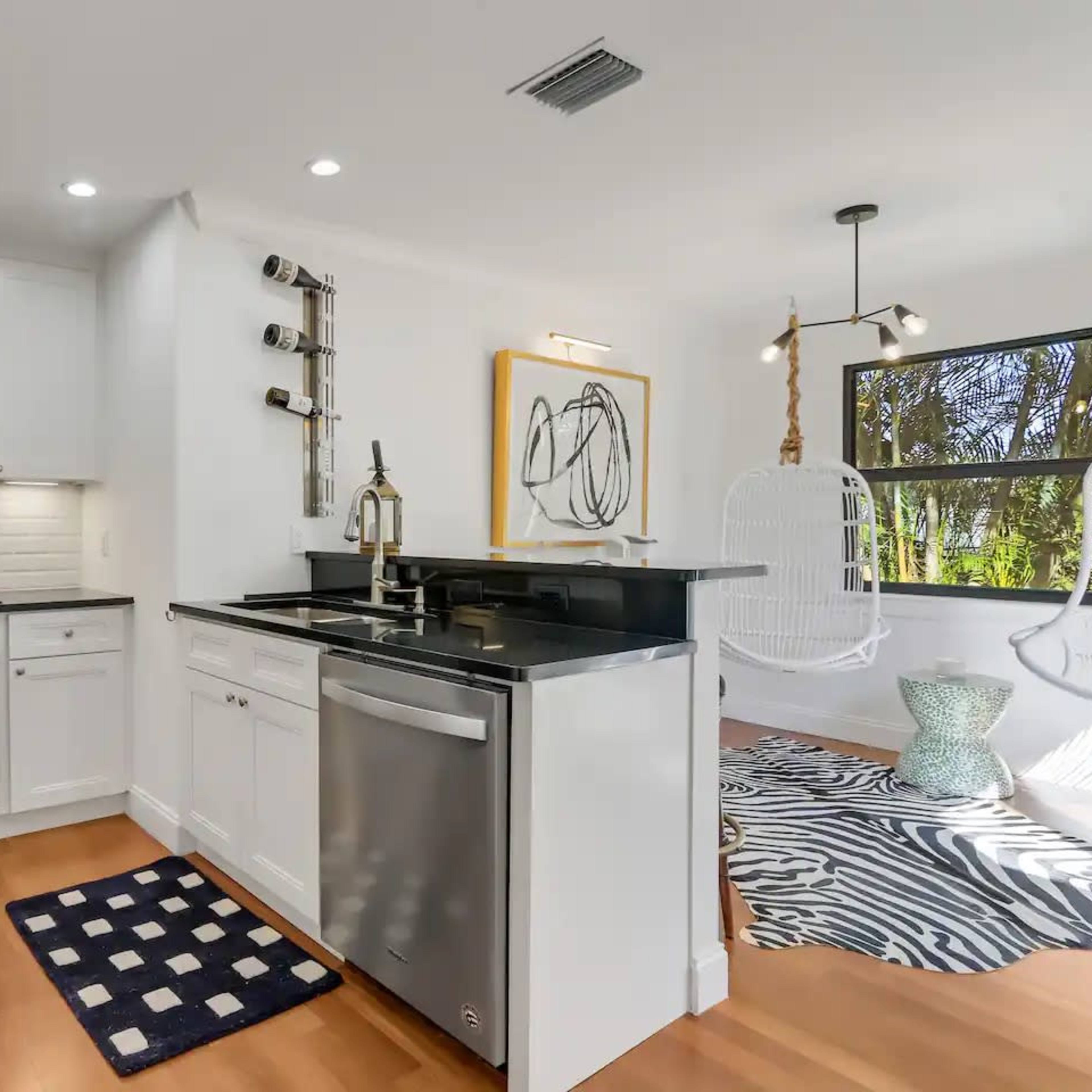 A modern kitchen with white cabinetry, stainless steel appliances, and a small dining area featuring hanging chairs and a decorative rug.