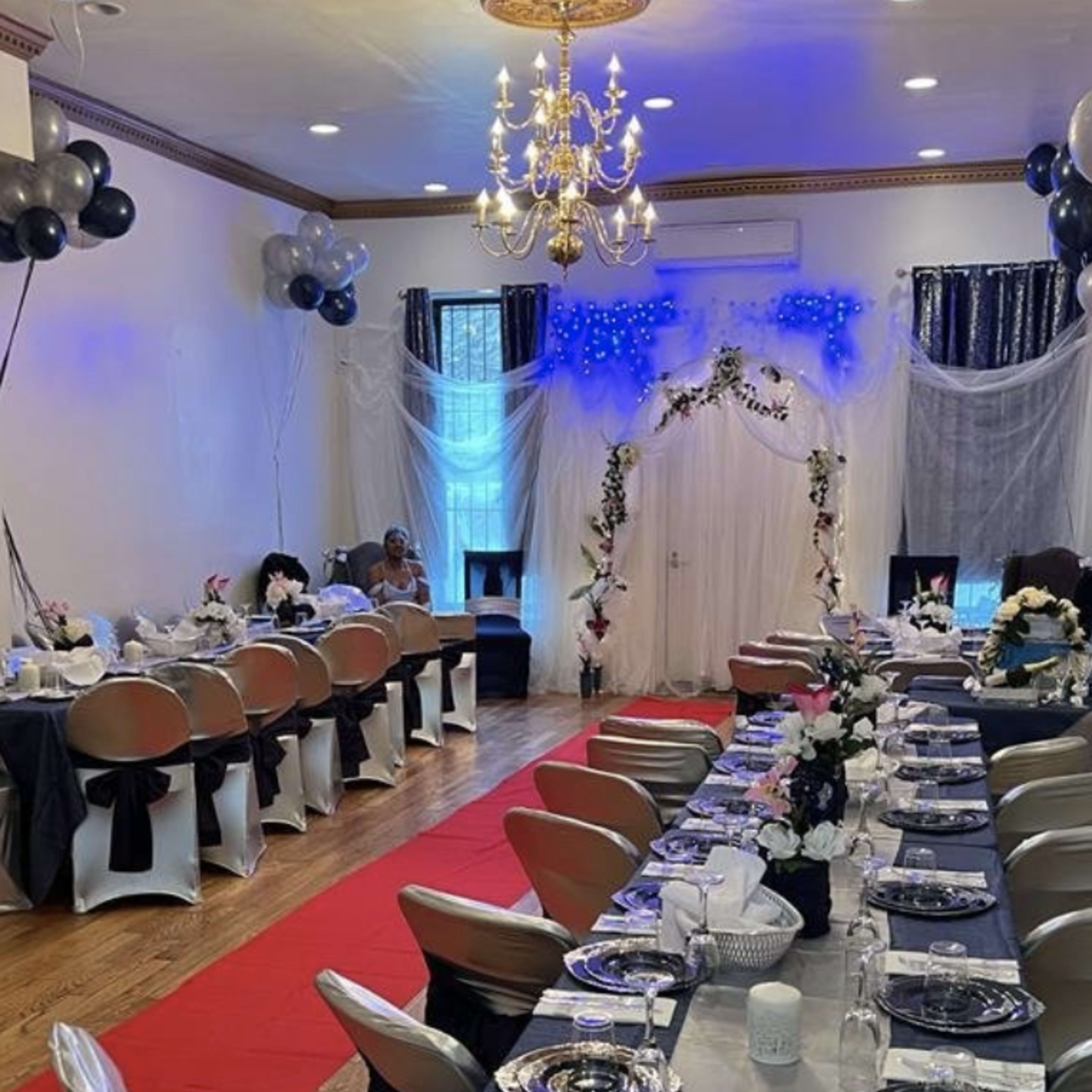 A decorated event space with tables set for a formal gathering, featuring a red carpet and floral arrangements.