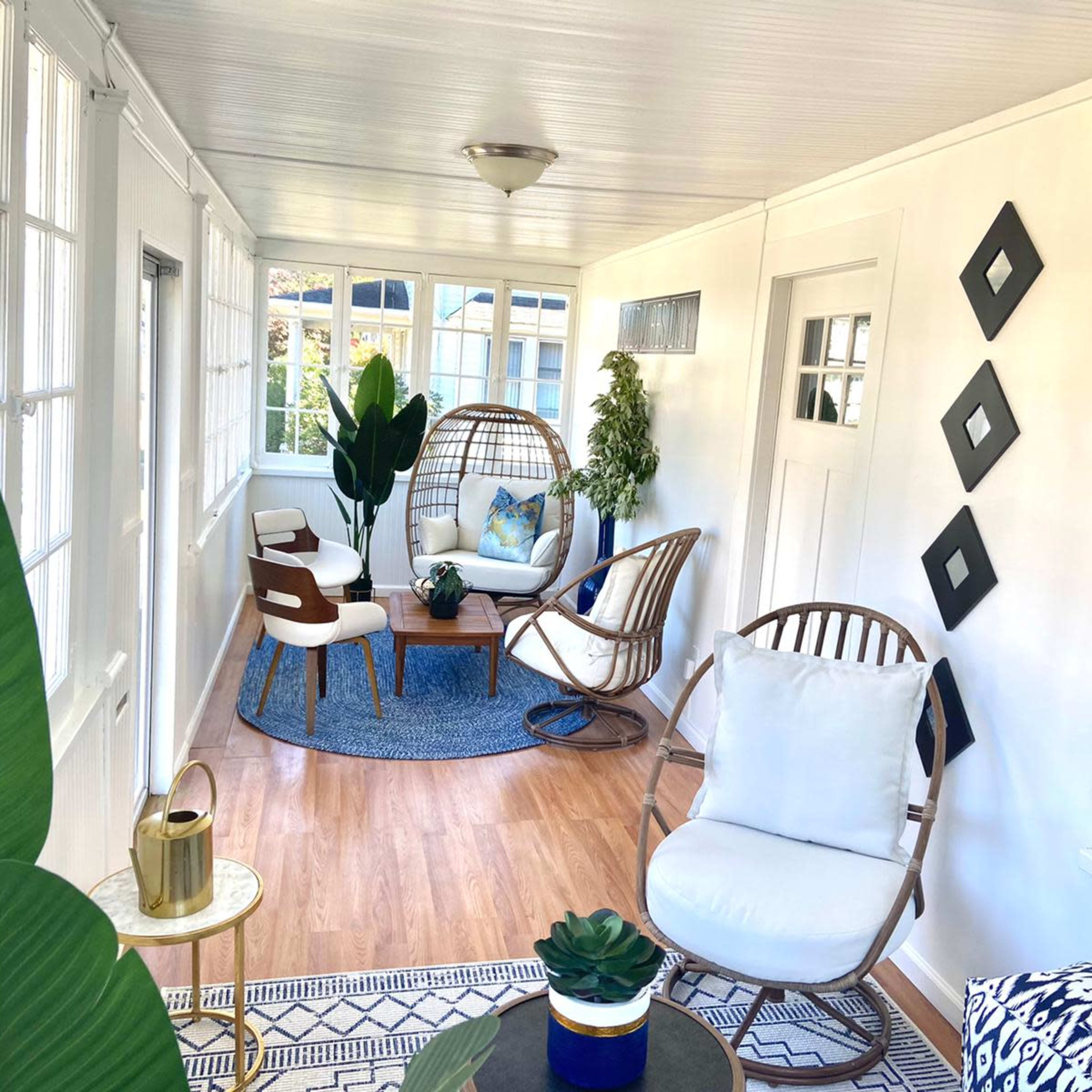 A bright sunroom with seating arrangements, plants, and decorative elements on the walls and furniture.