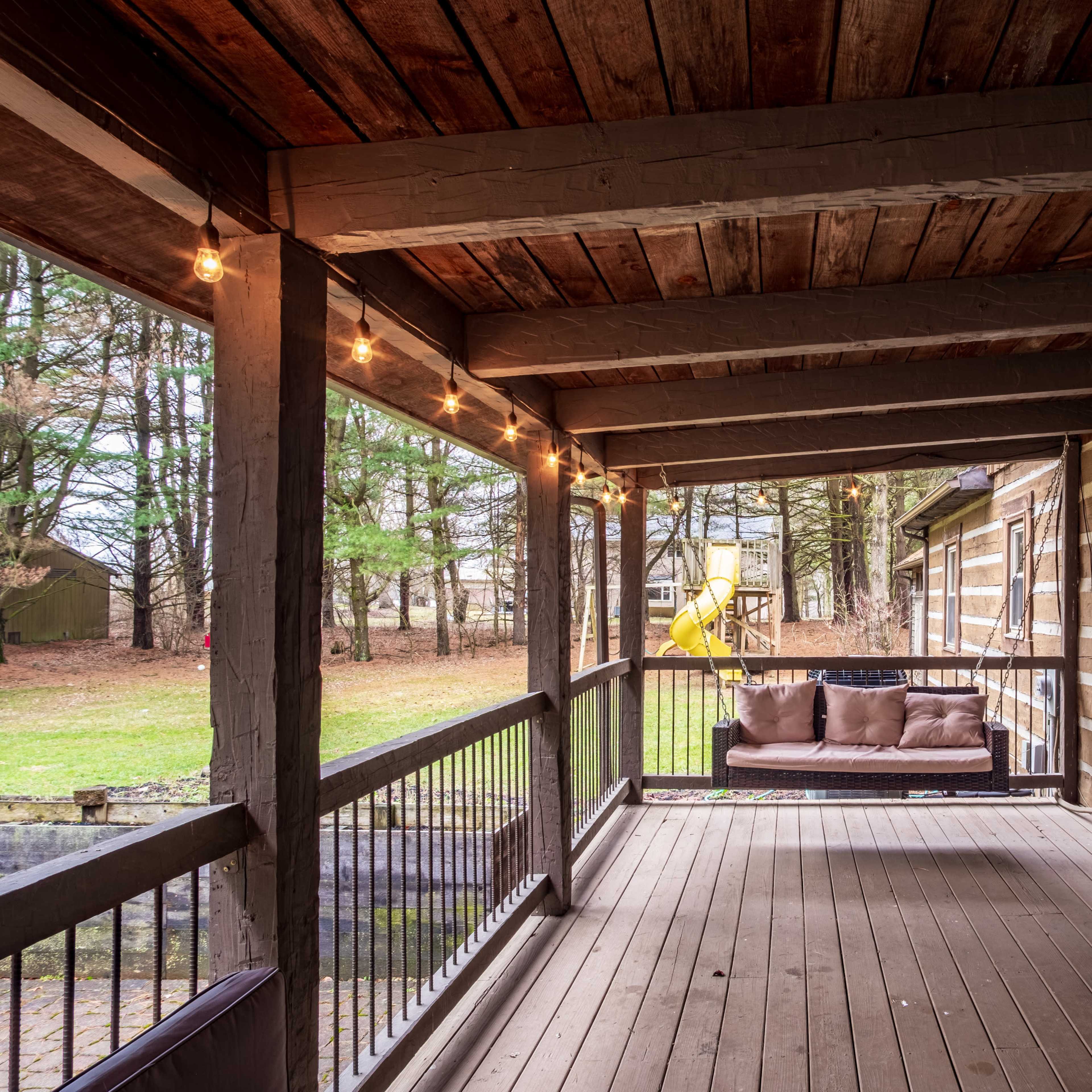 A wooden porch with a couch, string lights, and an adjacent grassy area.