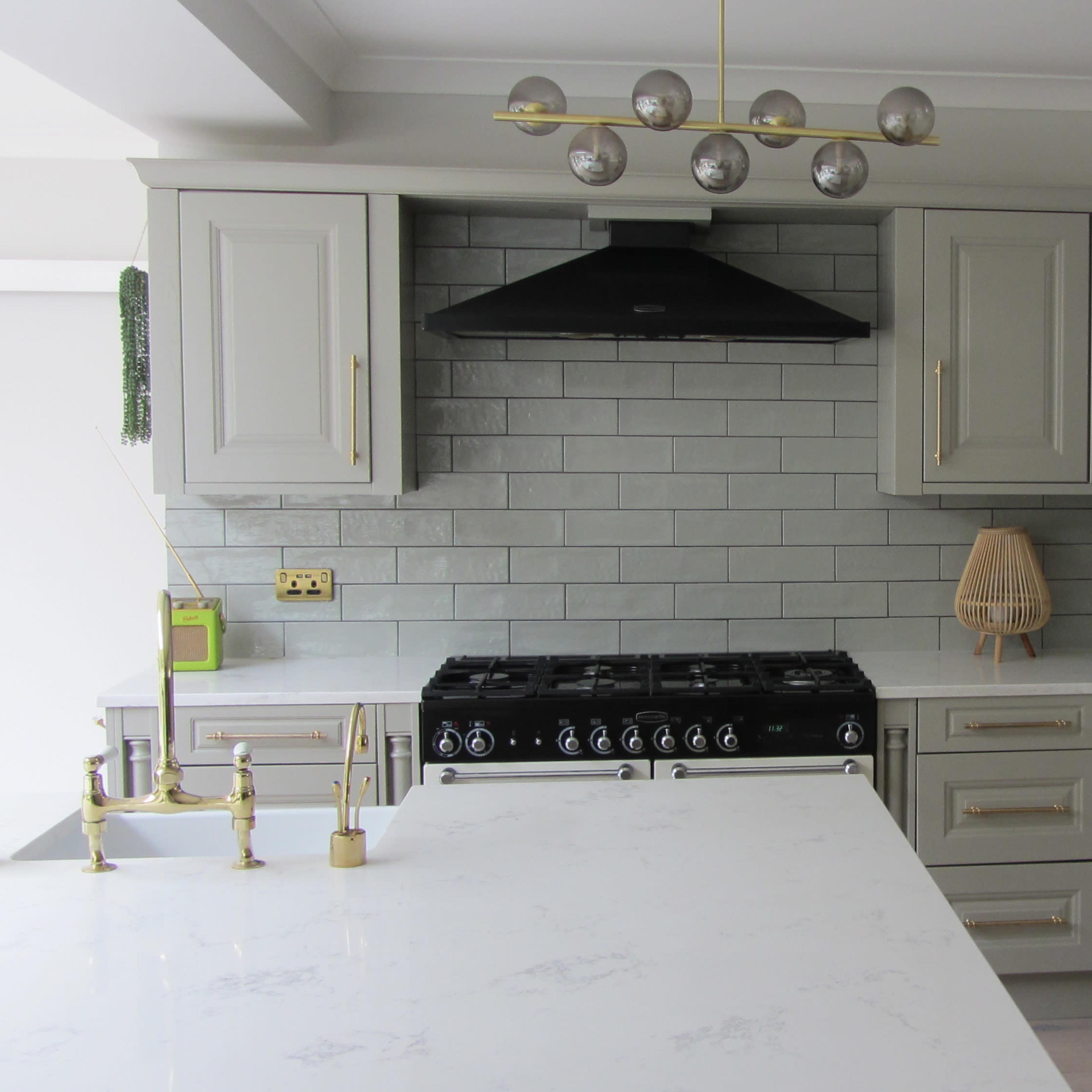 A modern kitchen featuring light gray cabinetry, a black gas stove, a quartz island, and a pendant light fixture with round bulbs.