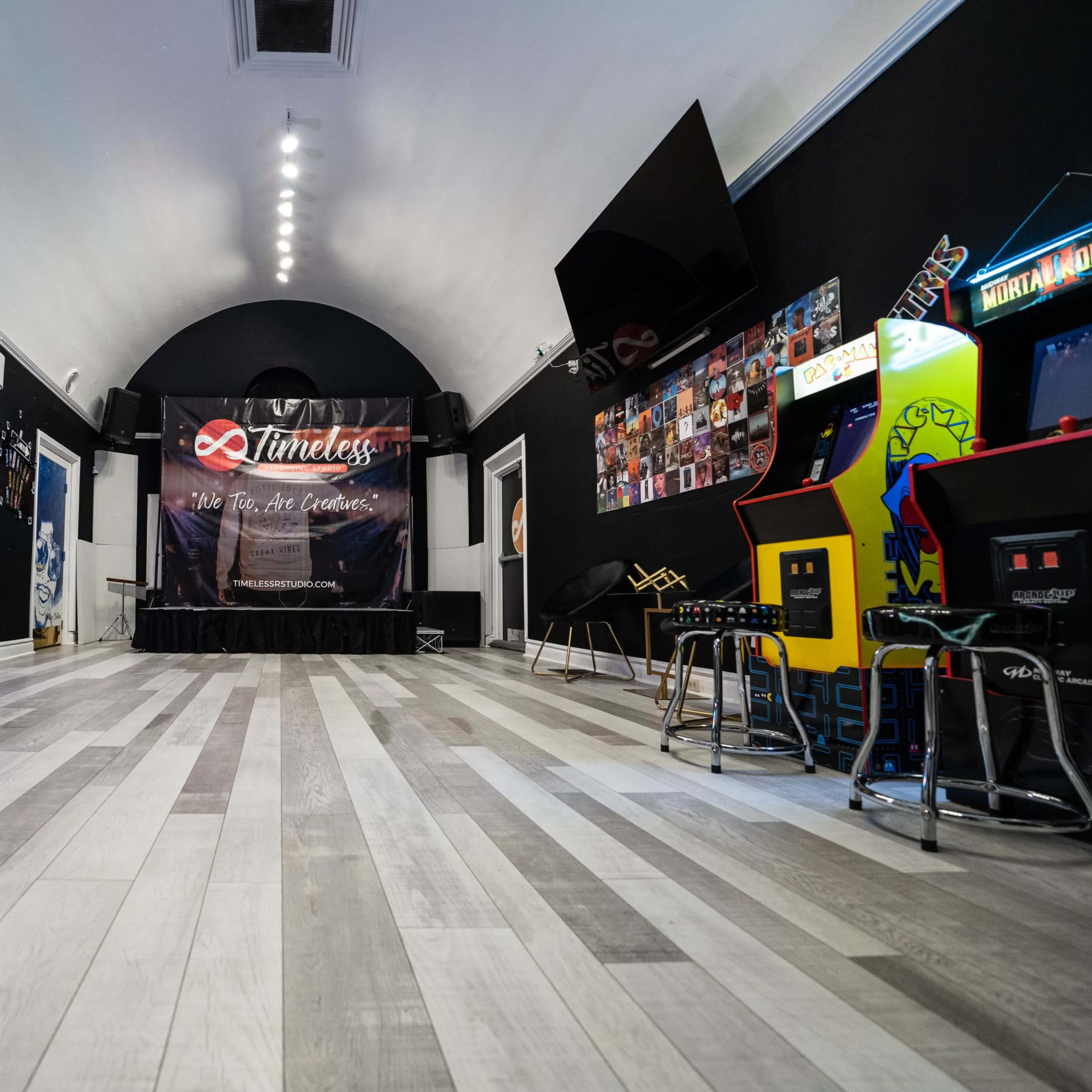 A spacious entertainment room with a stage at the front and arcade games on the sides.