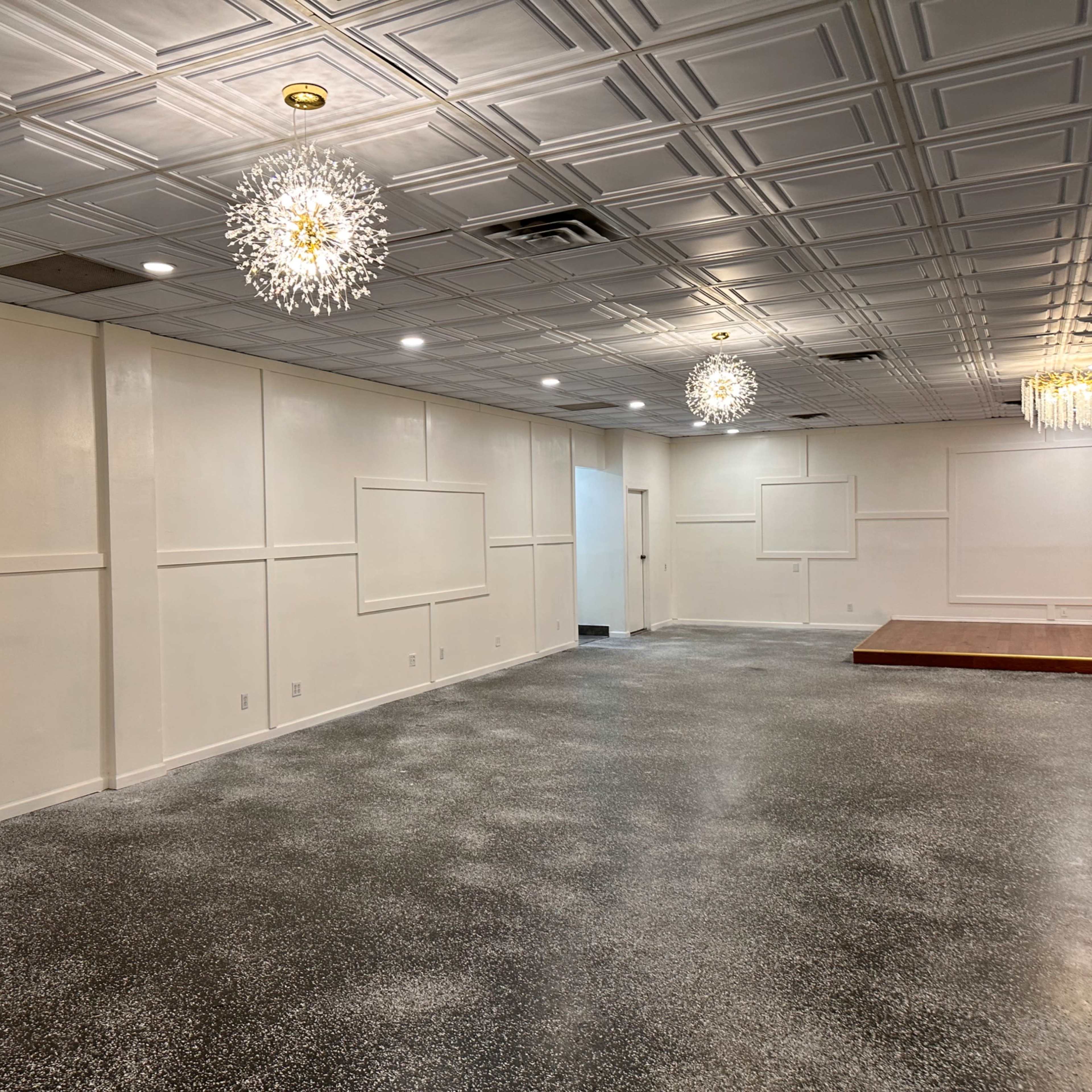 A spacious interior room with a polished floor, white walls featuring decorative panels, and several hanging light fixtures.
