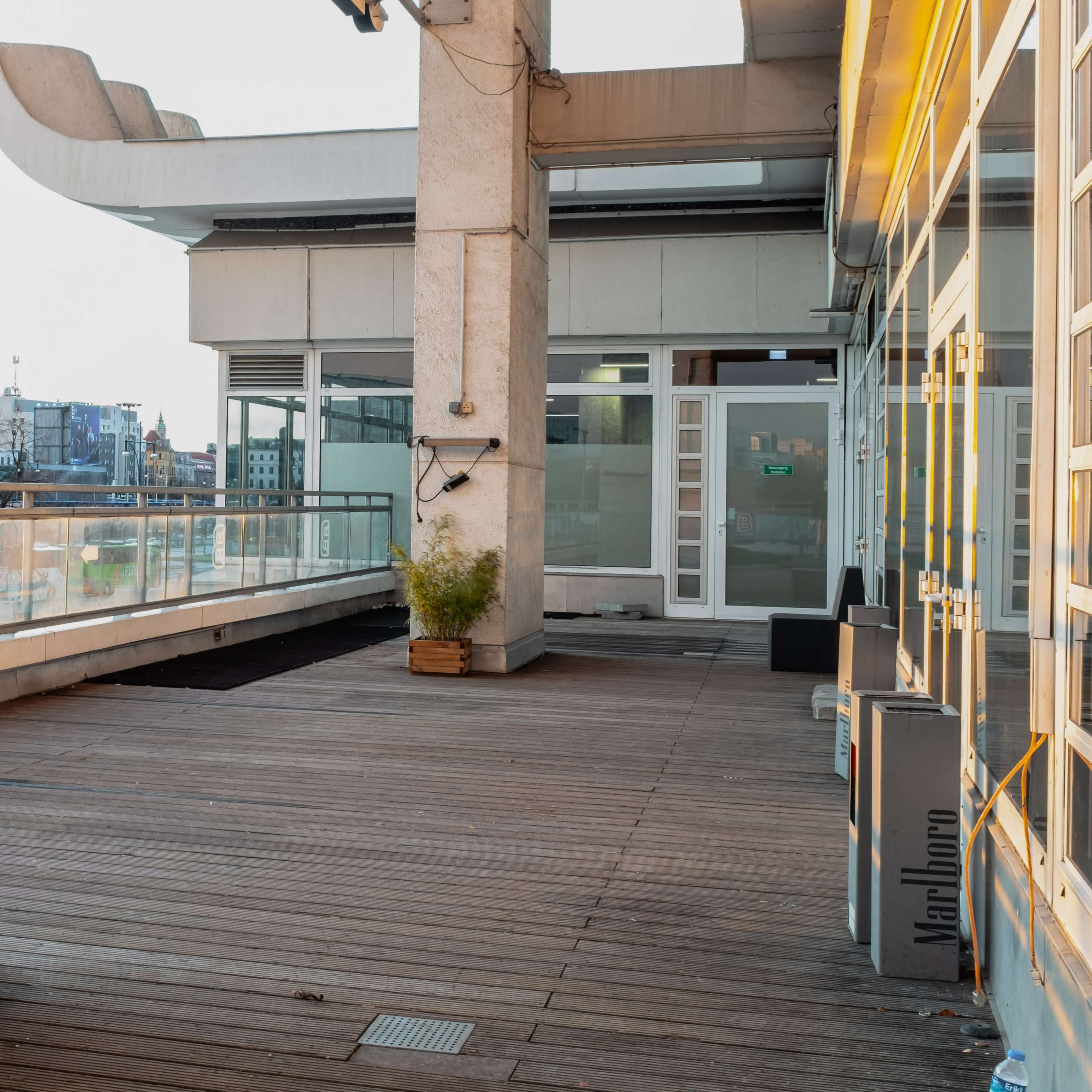 A modern terrace area with wooden flooring, concrete walls, and large windows overlooking a cityscape.