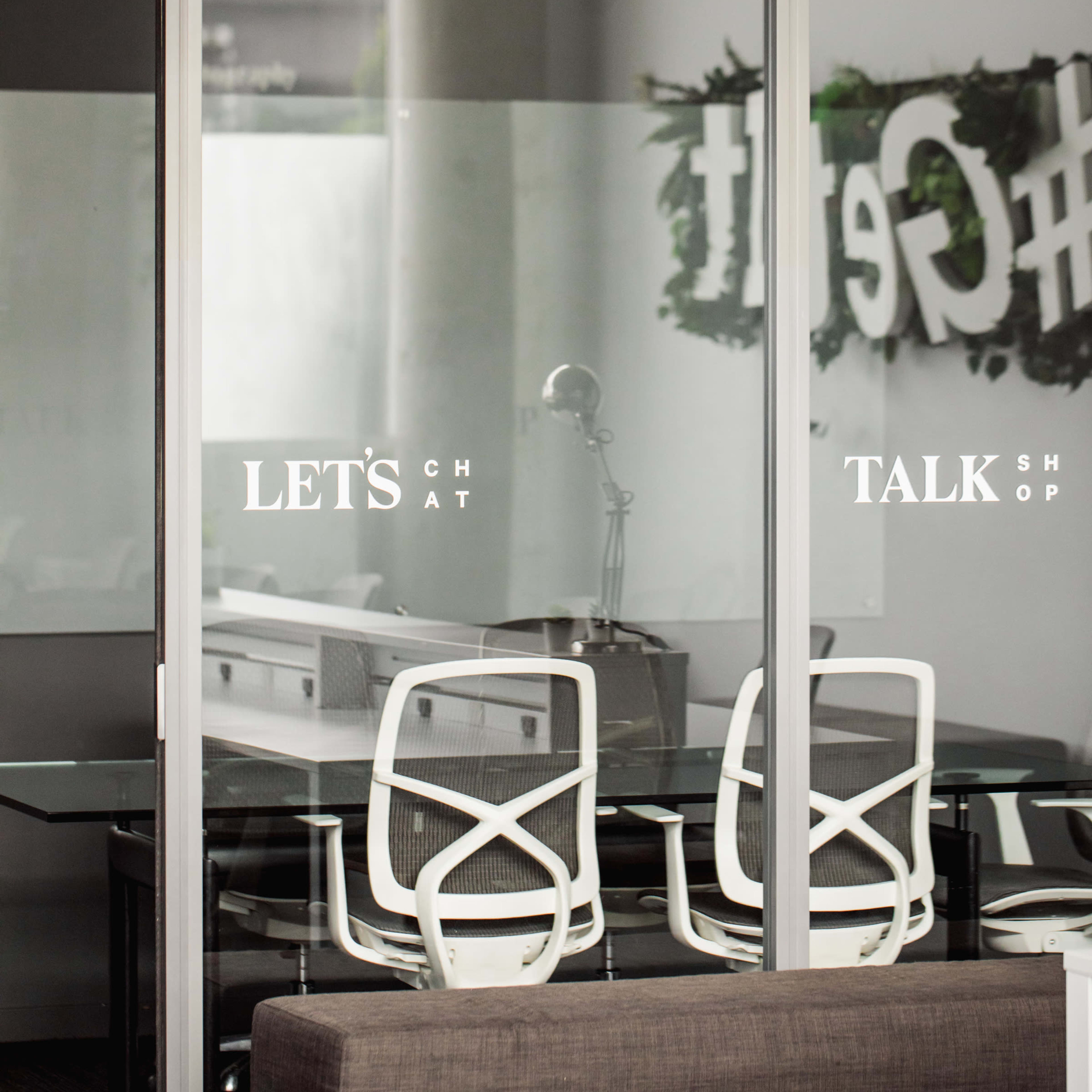 A modern office space with glass walls and a sign that reads "LET'S TALK SHOP" displayed on the door.