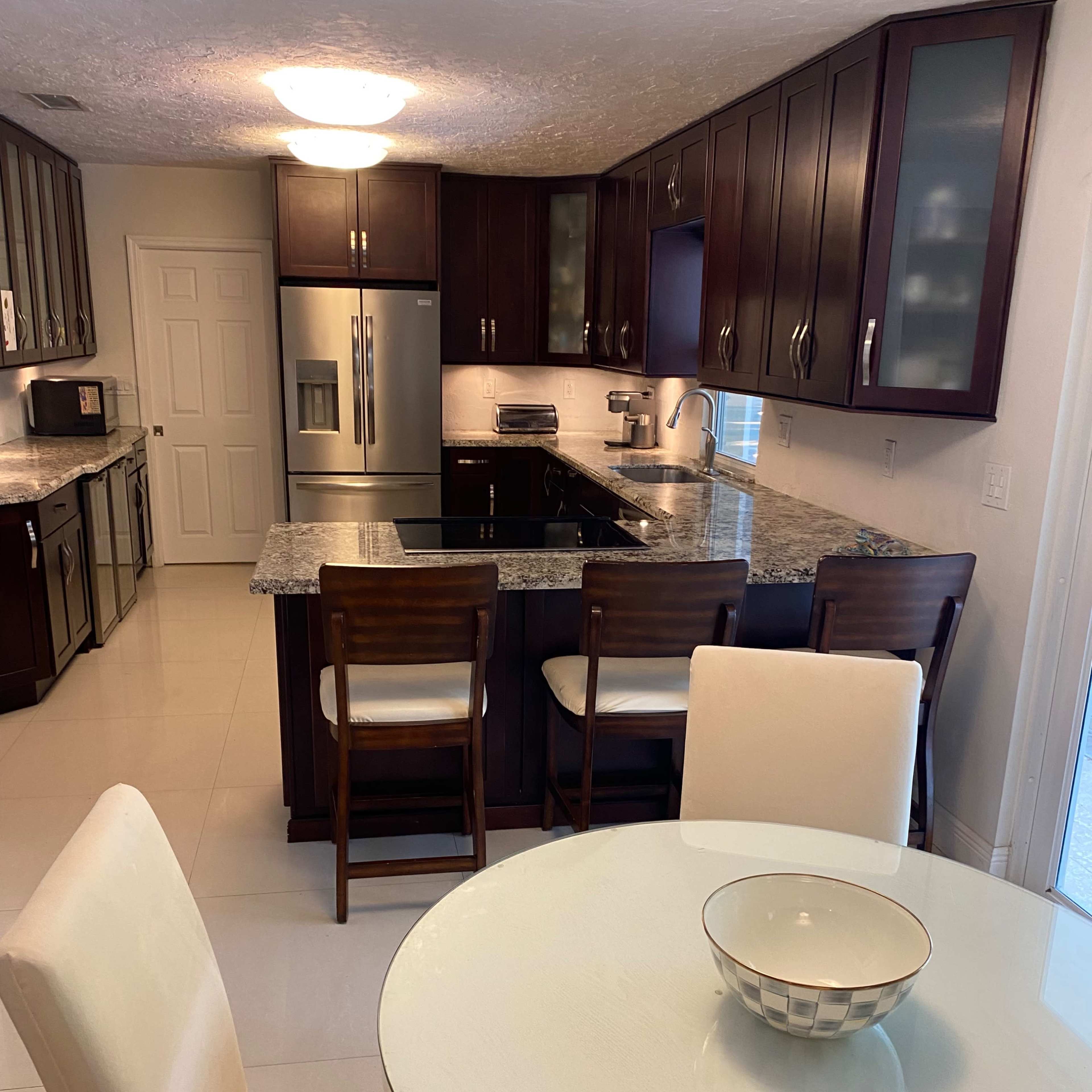 A modern kitchen with dark wooden cabinets, a large island with seating, and stainless steel appliances, alongside a round dining table with a bowl in the center.