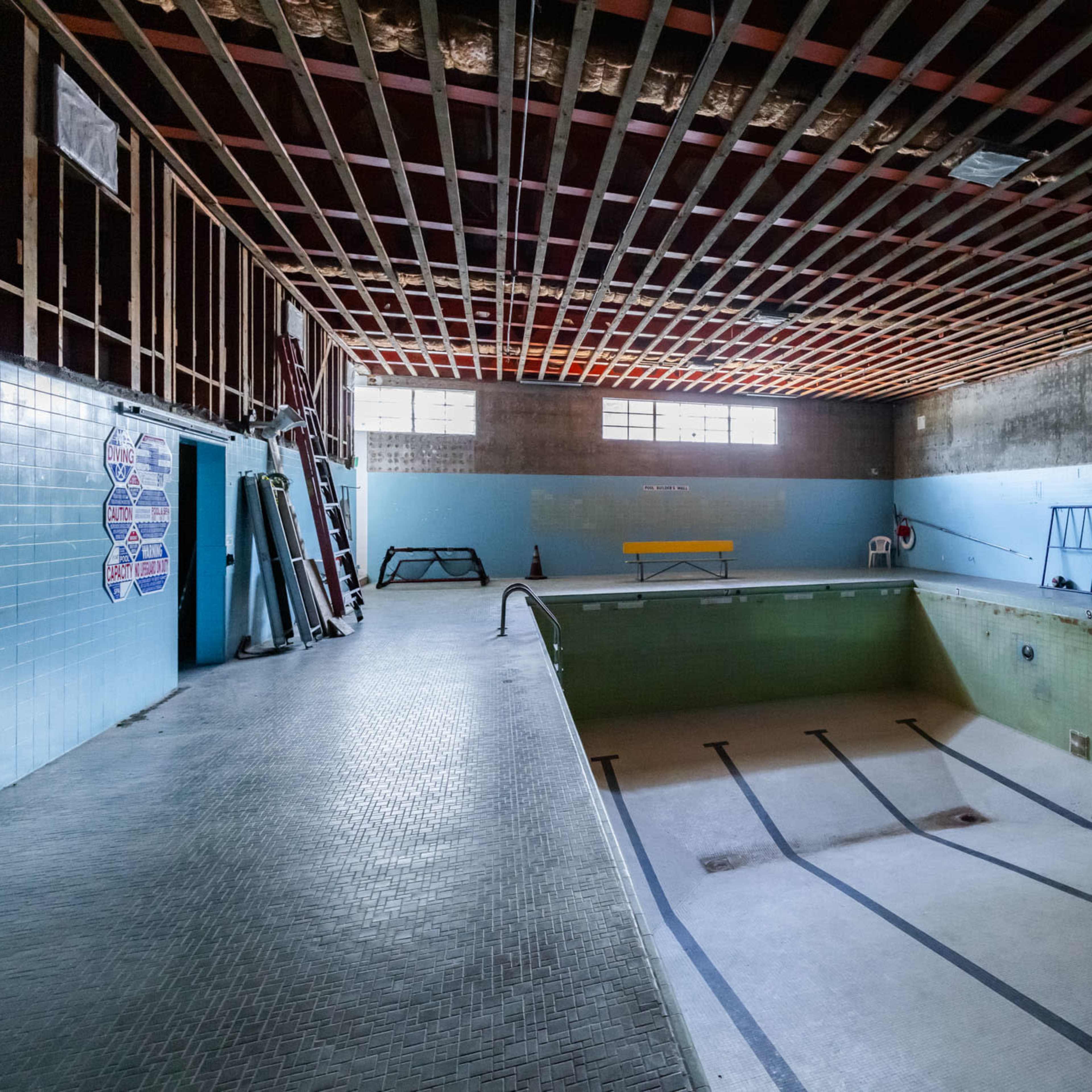 An empty indoor swimming pool with bare walls and exposed ceiling beams.
