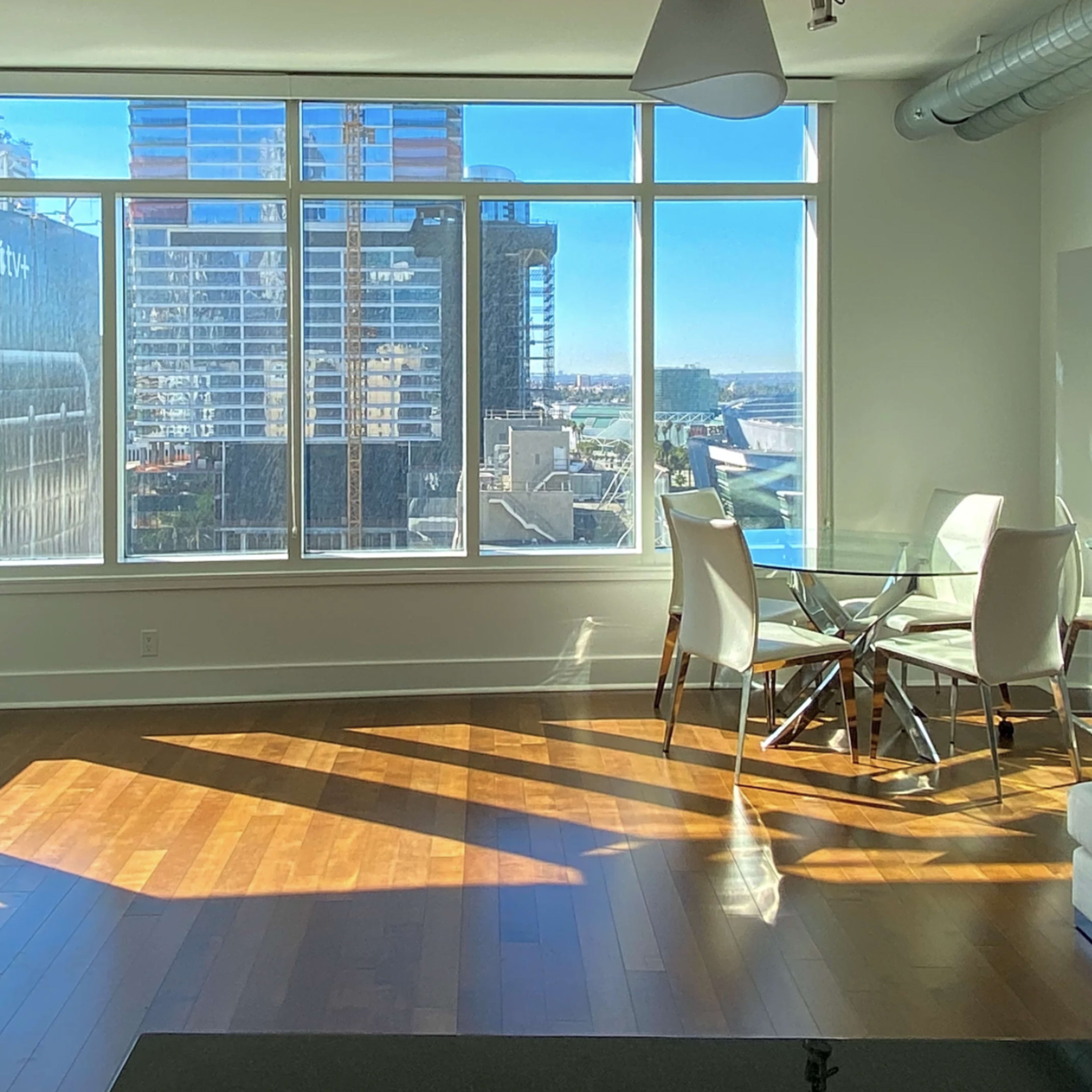 A modern living space features large windows with city views and sunlight casting shadows on the wooden floor.