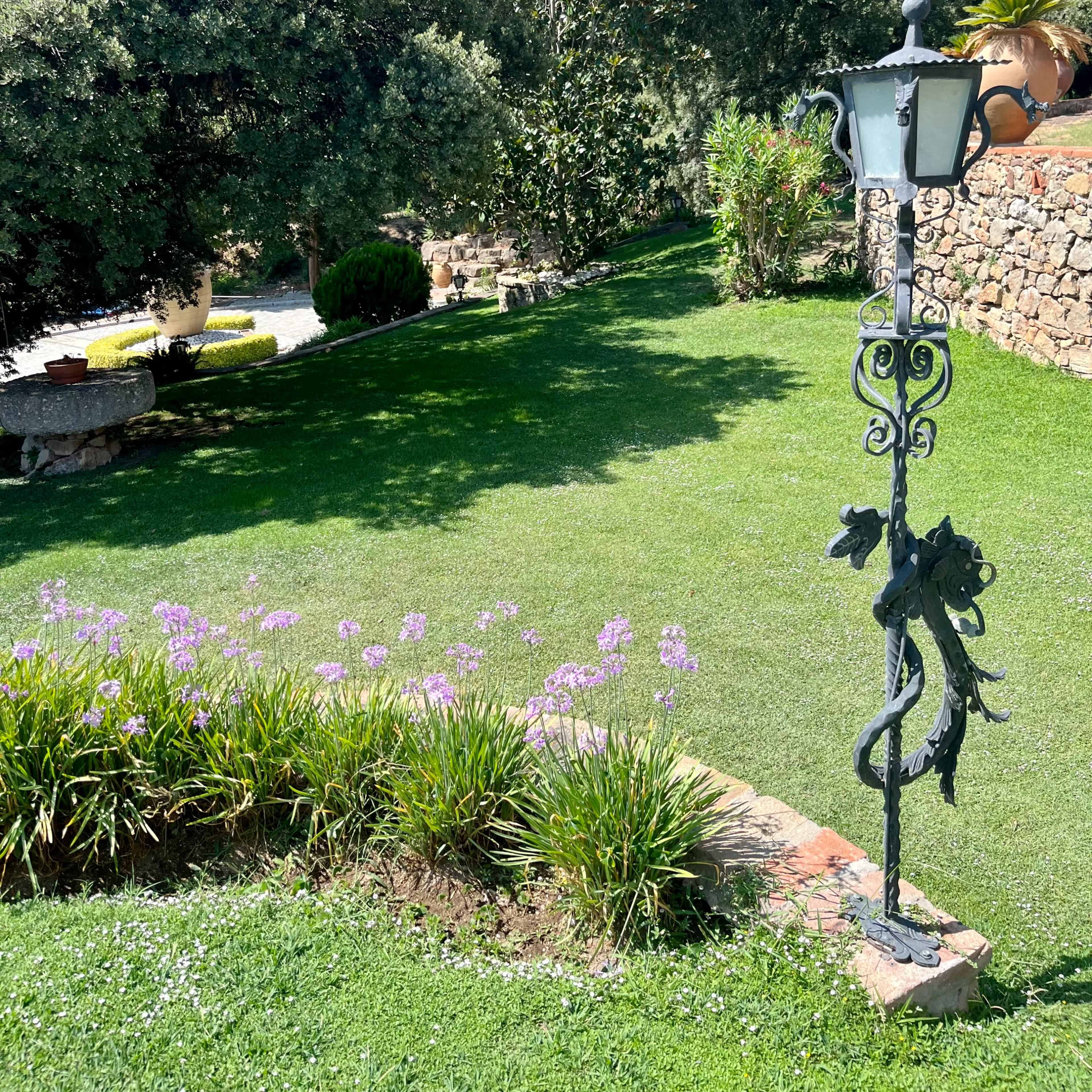 A decorative lamppost stands amidst a landscaped garden featuring lush green grass and patches of flowers.