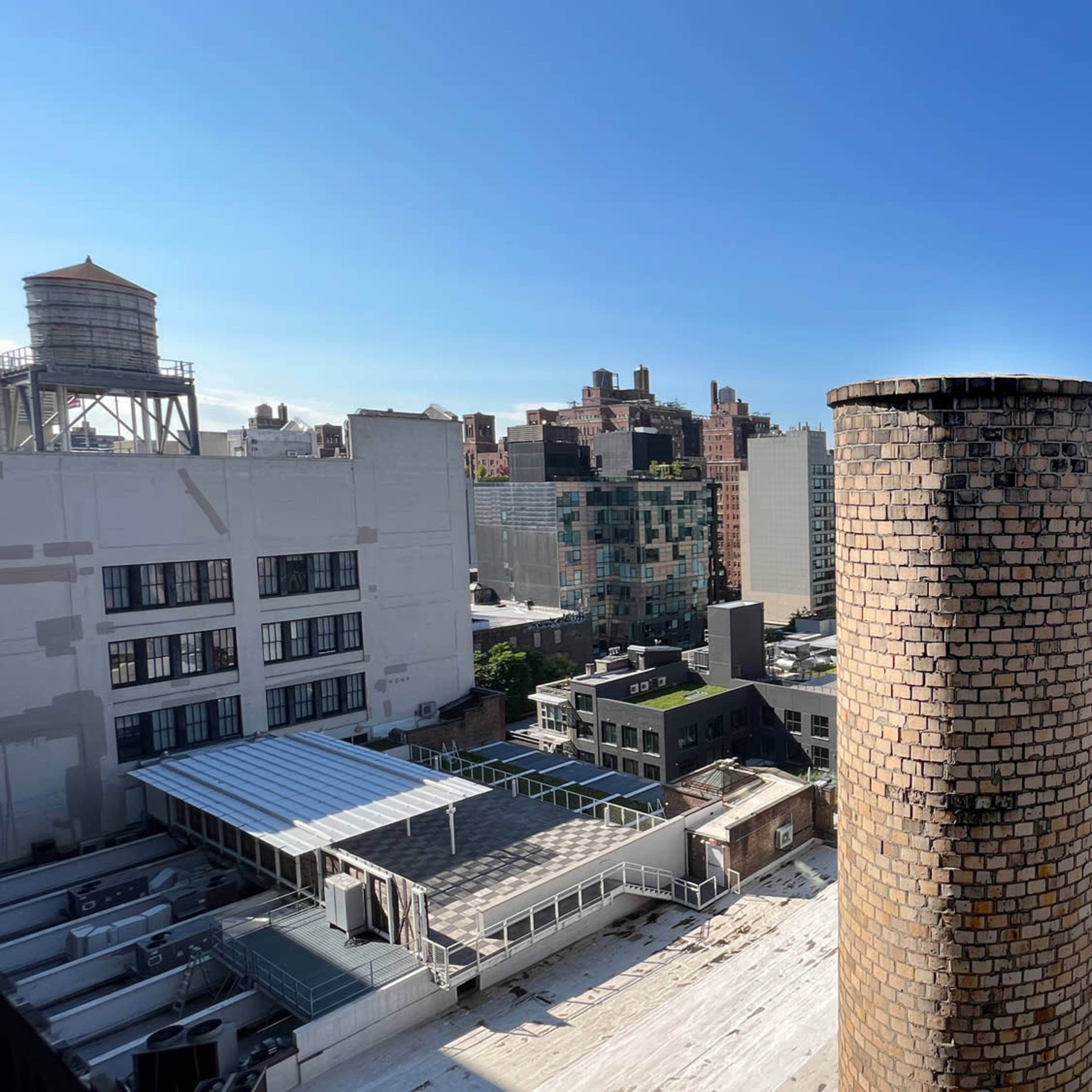A city skyline featuring a large brick chimney in the foreground, surrounded by various modern buildings and a clear blue sky.