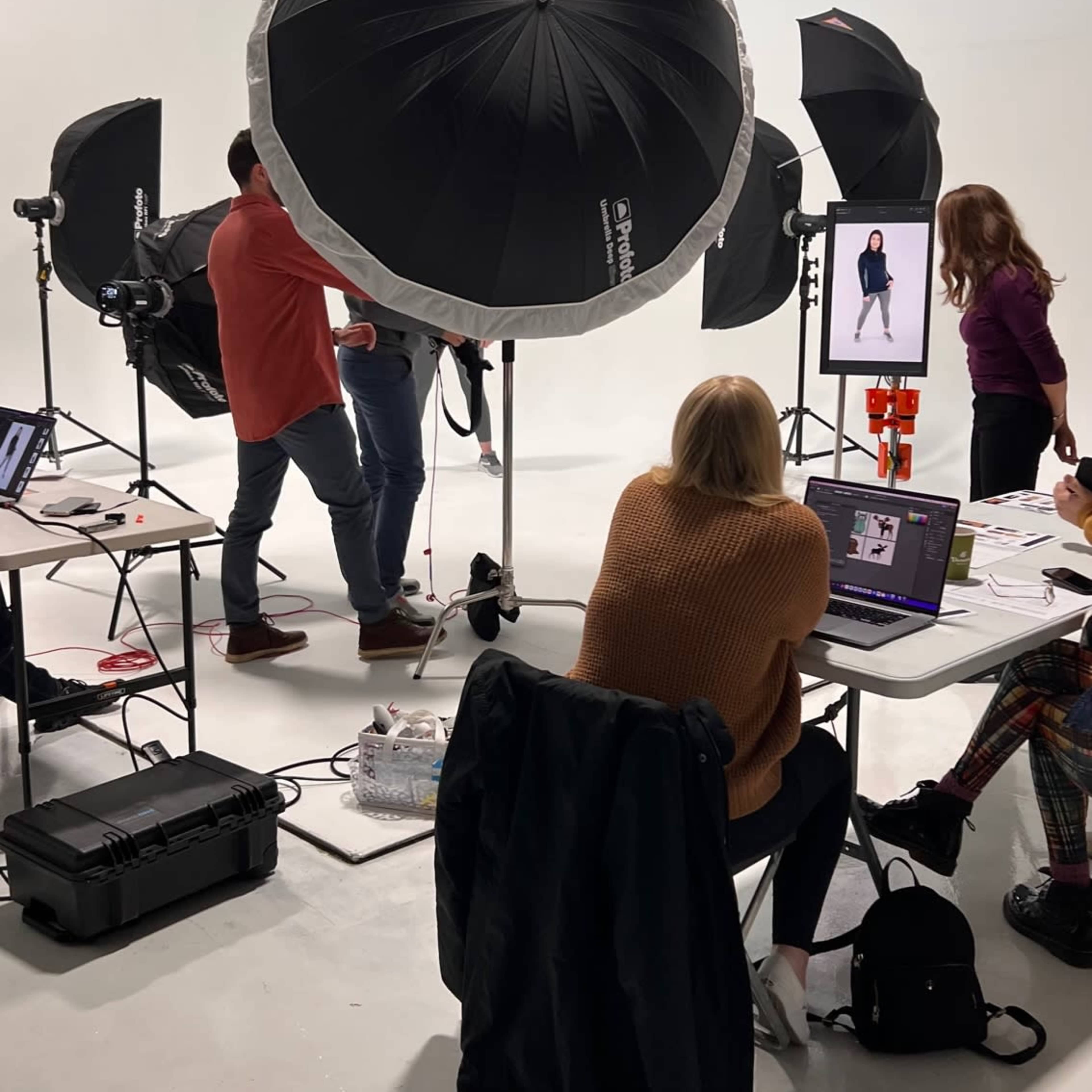 A photo shoot takes place in a studio with several lighting setups and a team of people collaborating around tables.