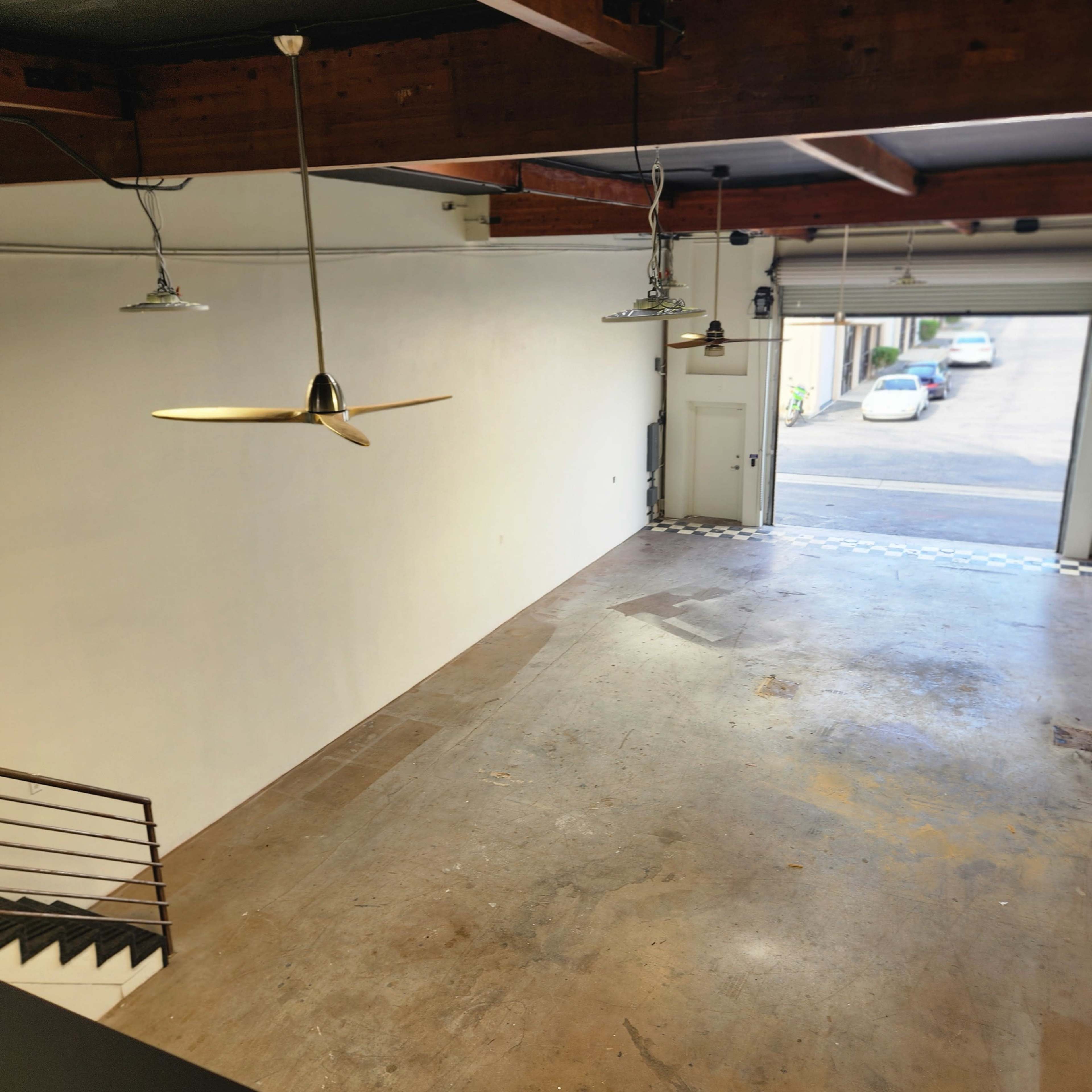 A spacious room with a concrete floor and large entrance doors, leading to a parking area outside.