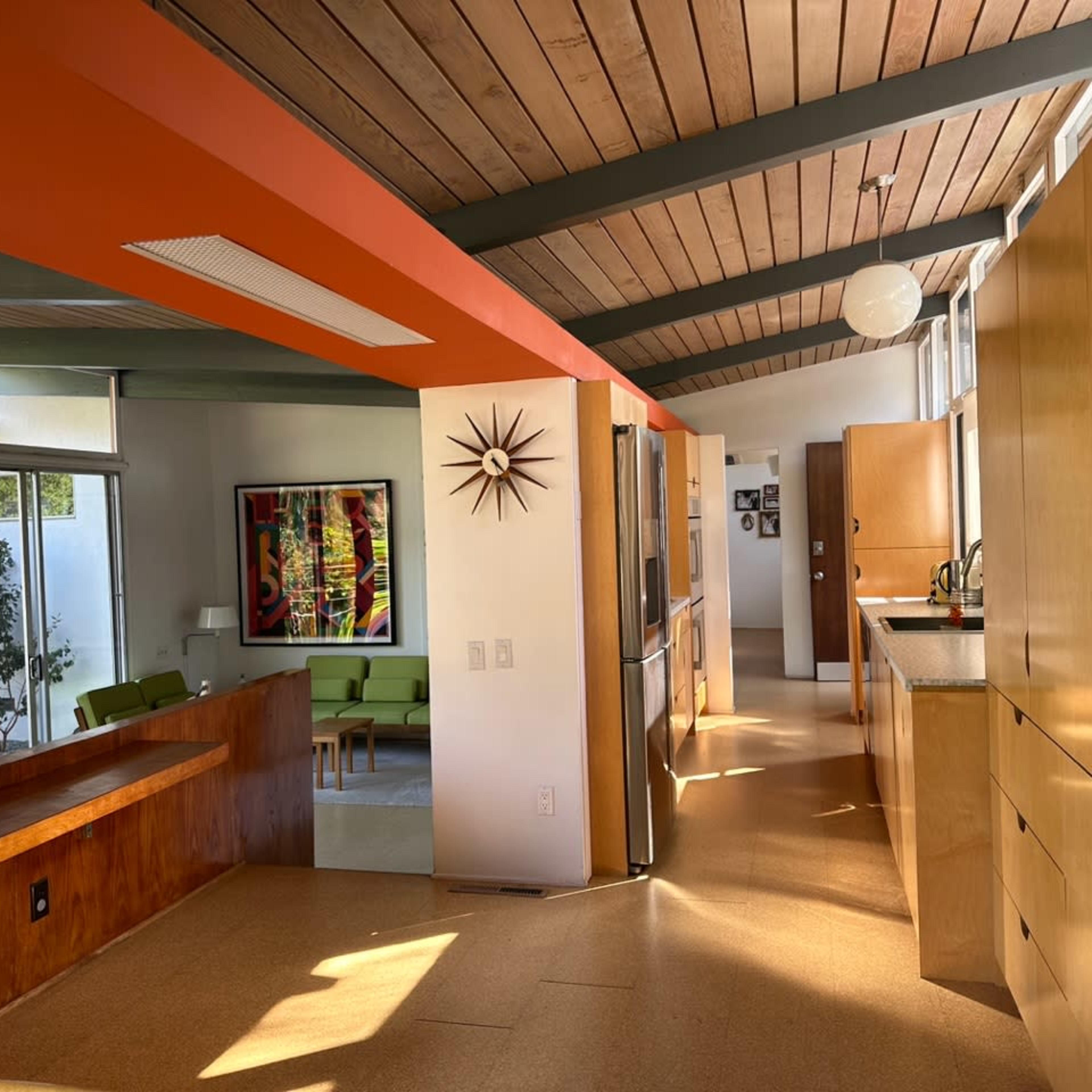 A modern interior space with wooden ceilings, an open layout, and kitchen areas featuring wood cabinets and bright orange accents.
