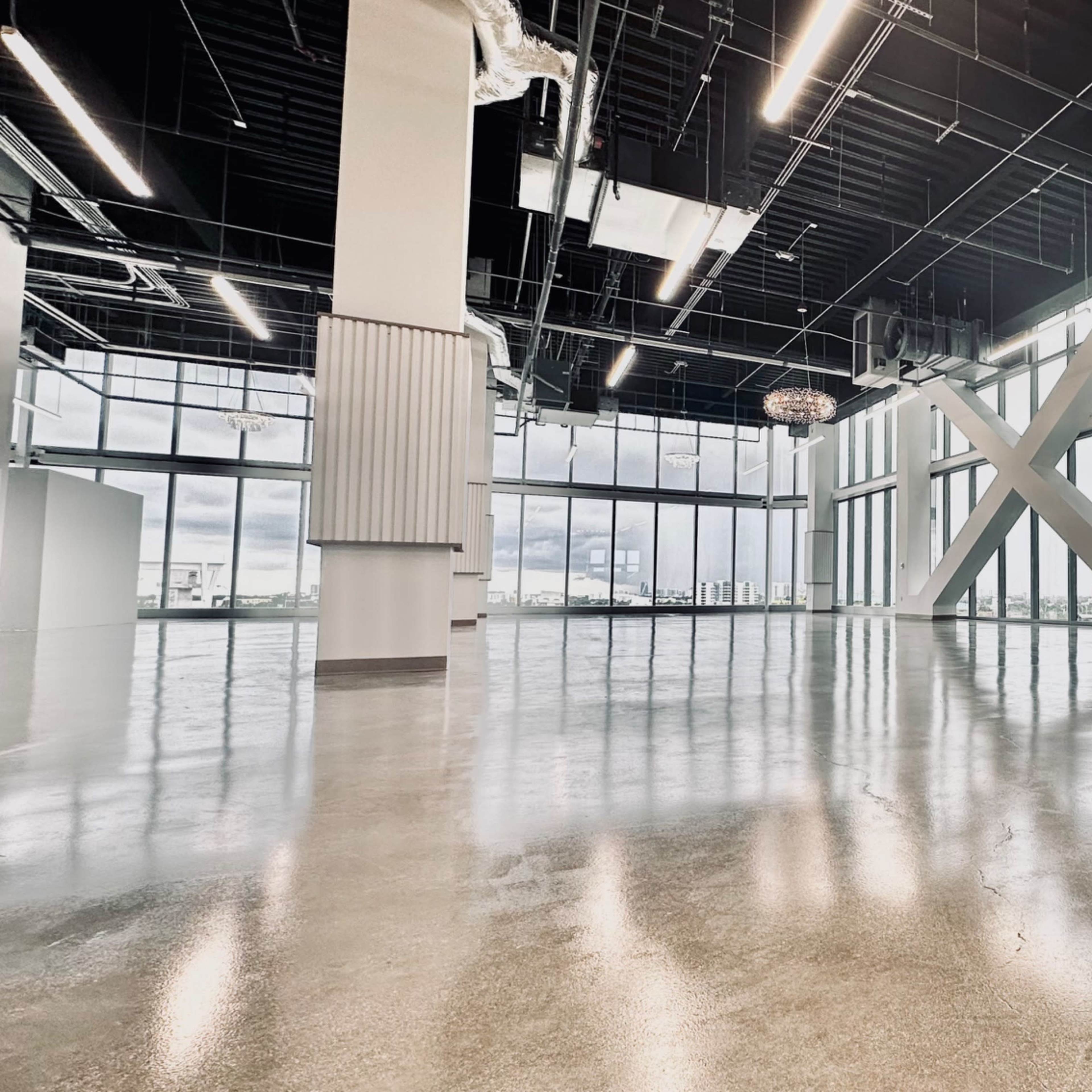 An empty commercial interior space with polished concrete flooring, large windows, and modern lighting fixtures.