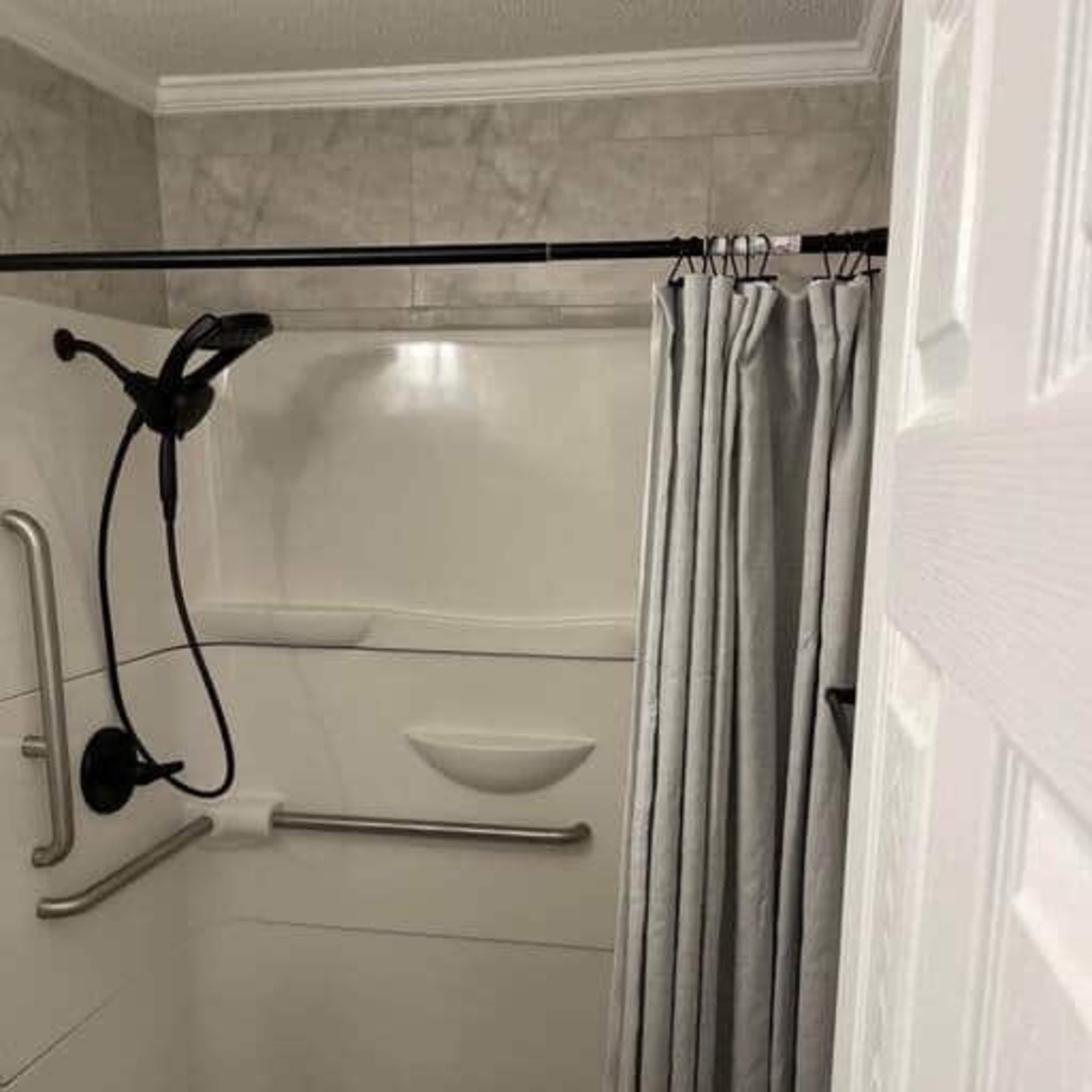 A small shower area with a grab bar, a showerhead mounted on a sliding rail, and a fabric shower curtain.