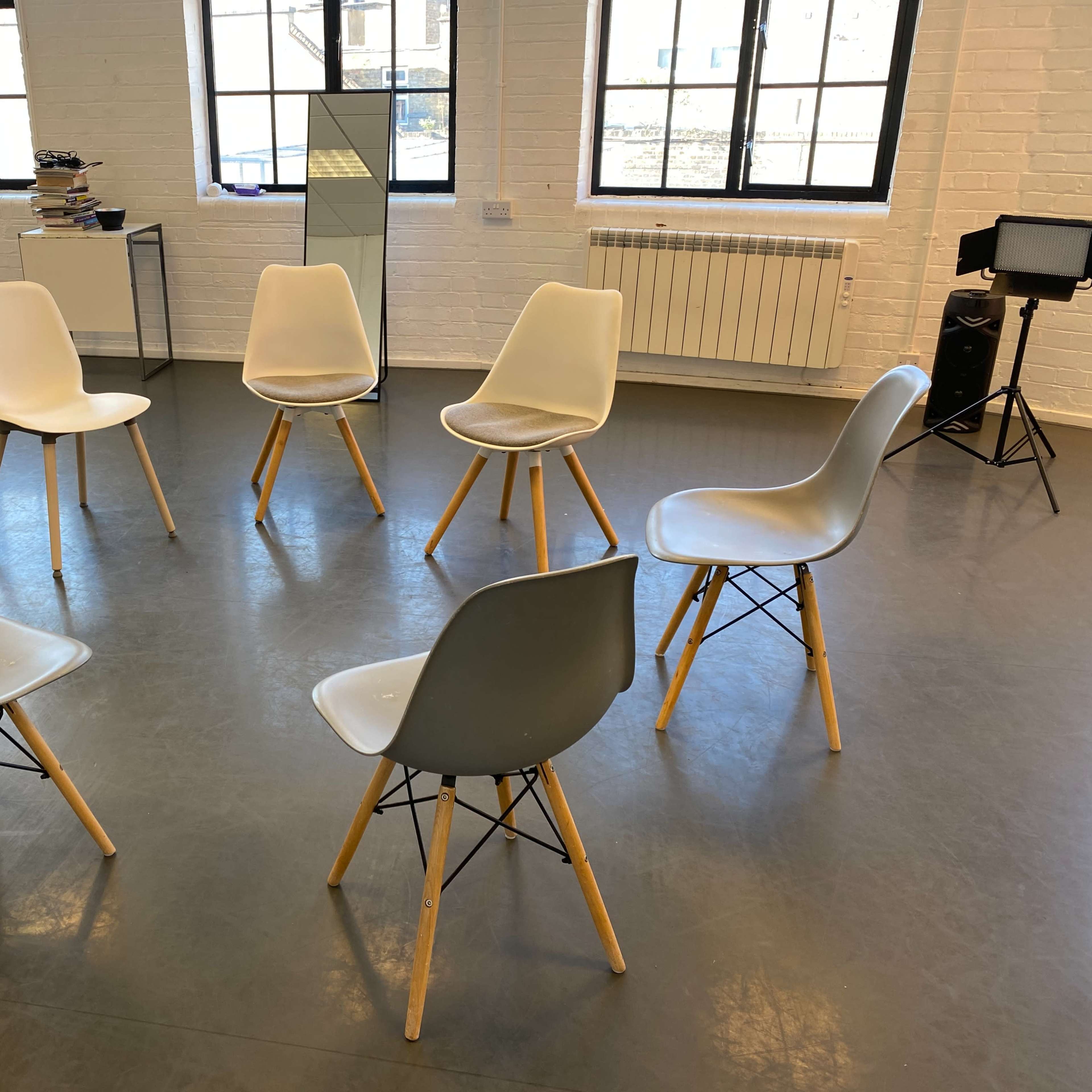 Eight chairs are arranged in a circle on a gray floor in a well-lit room with large windows.