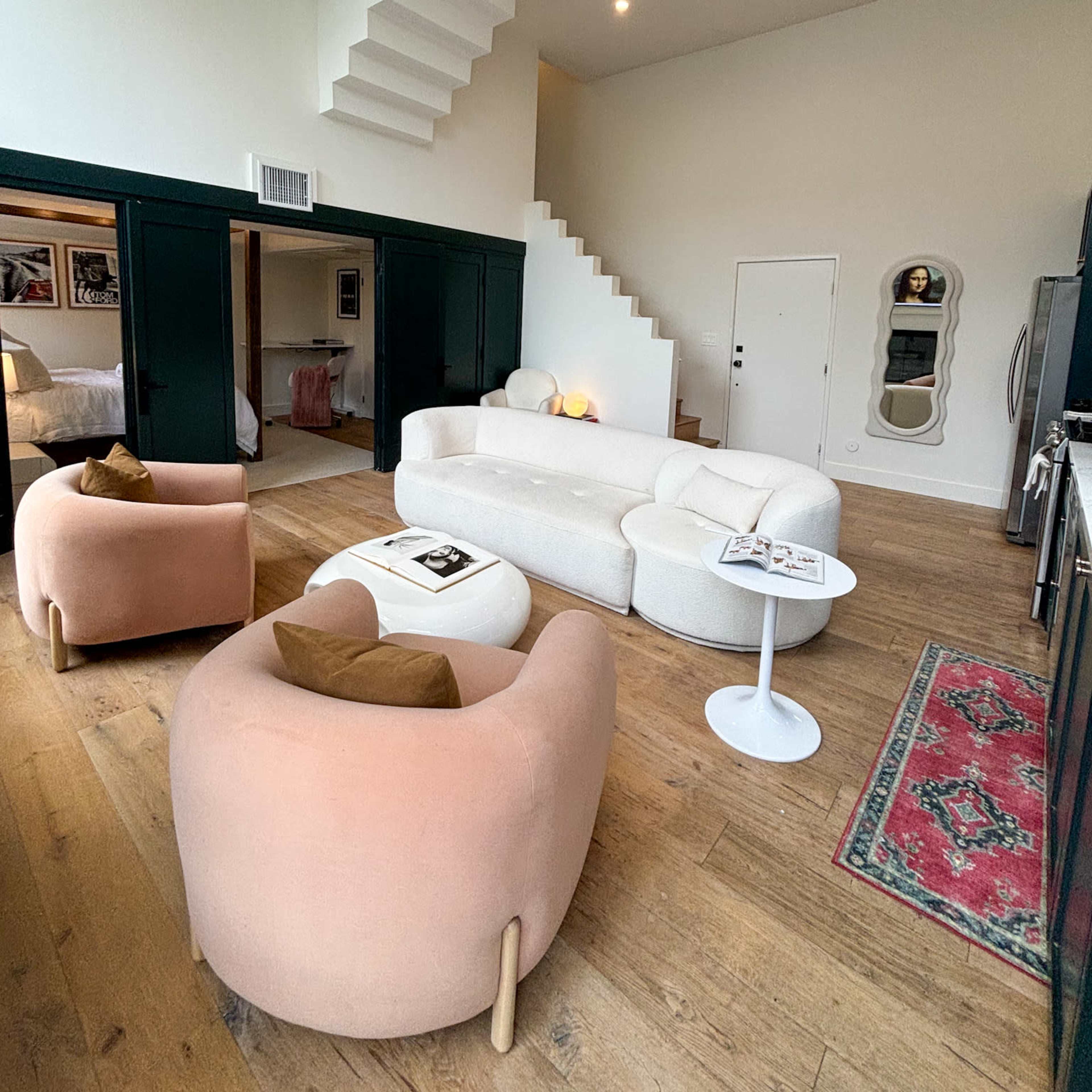 A modern living room with two rounded seating chairs, a low table, and a staircase leading to an upper level, all set against a white and dark green color scheme.
