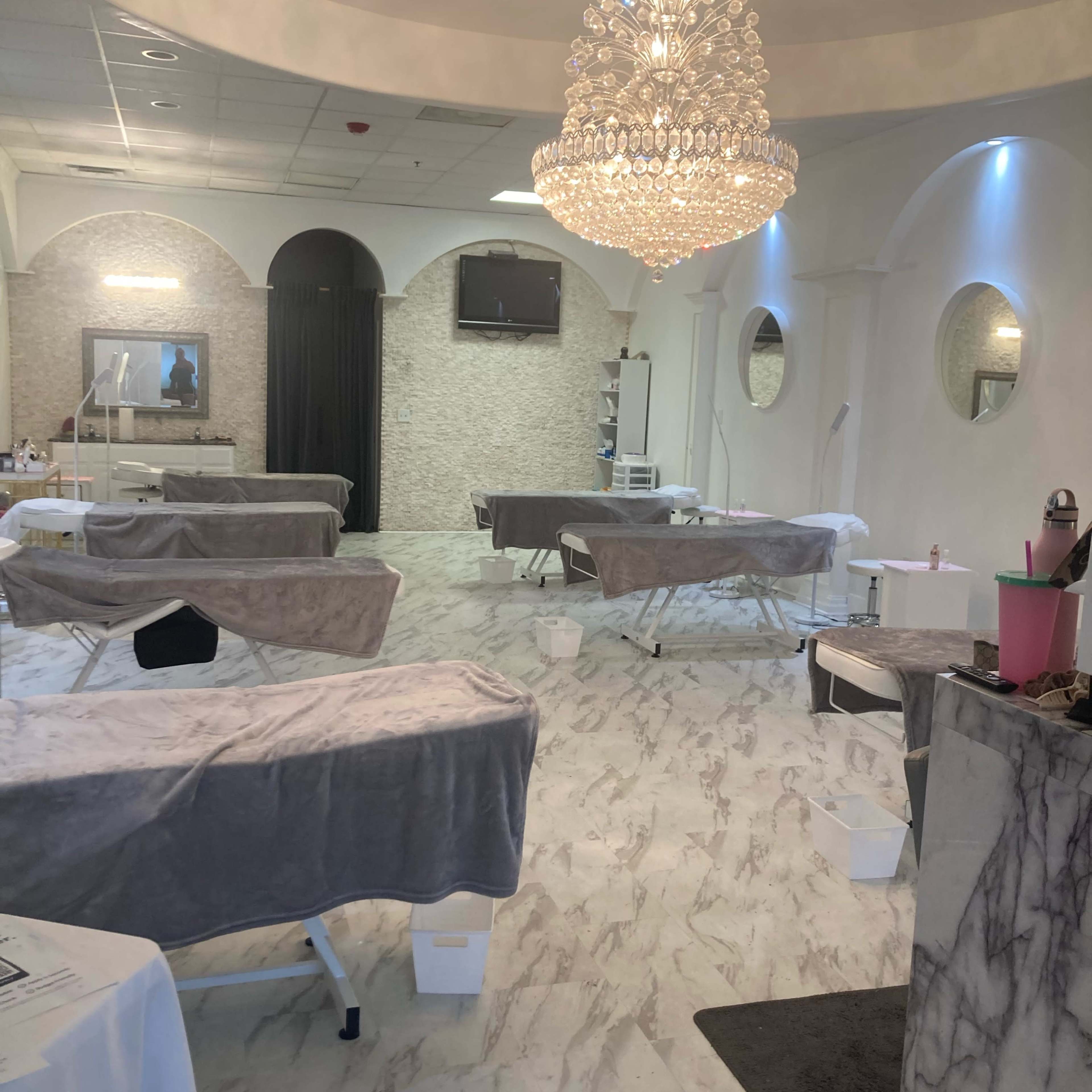 A spacious spa treatment room with several massage tables, elegant decor, and a chandelier overhead.