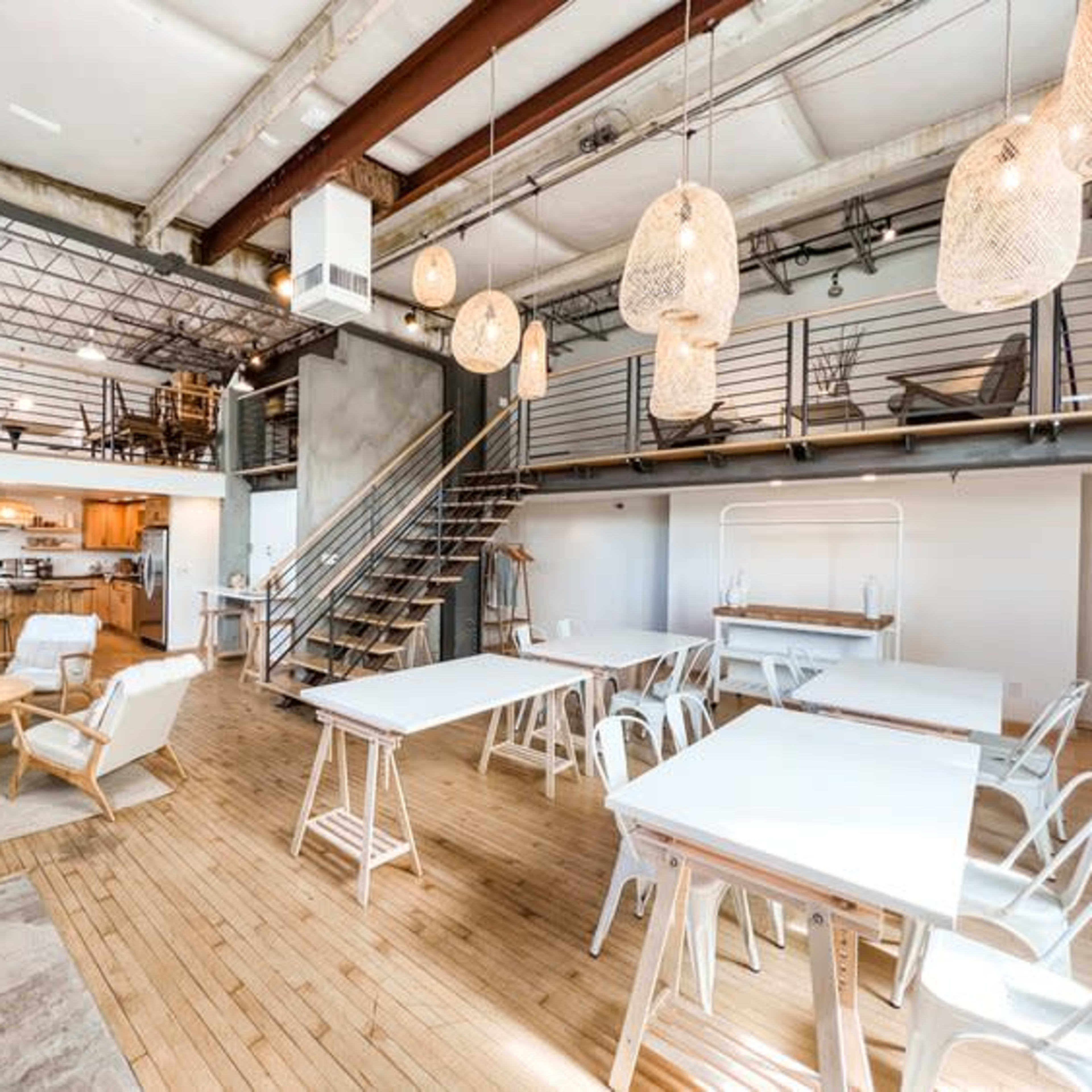 A spacious, modern interior with wooden floors, a kitchen area, and several tables surrounded by unique light fixtures.