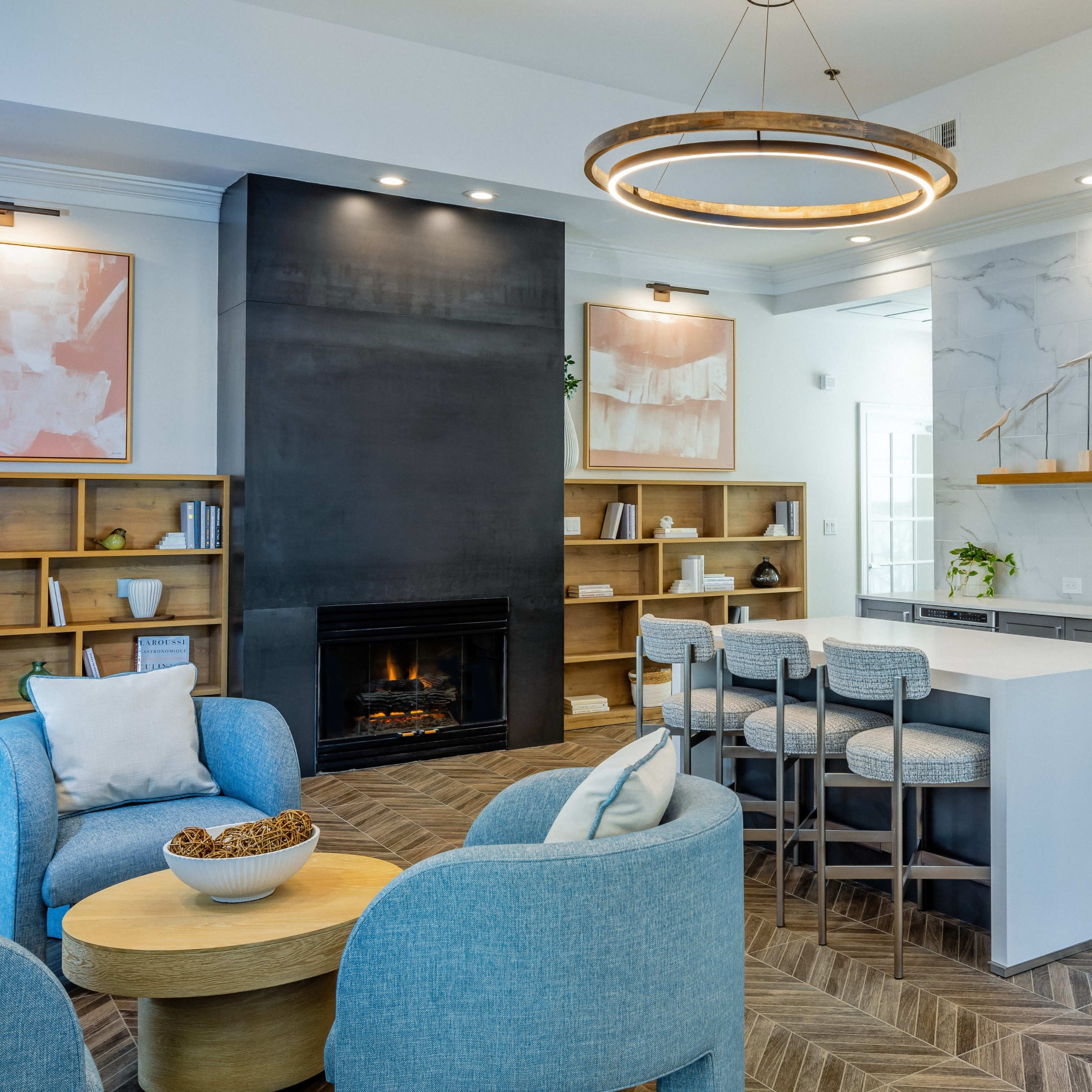 A modern living space featuring a sleek kitchen with gray cabinetry, a large island with seating, a fireplace, and a cozy seating area with light blue chairs.