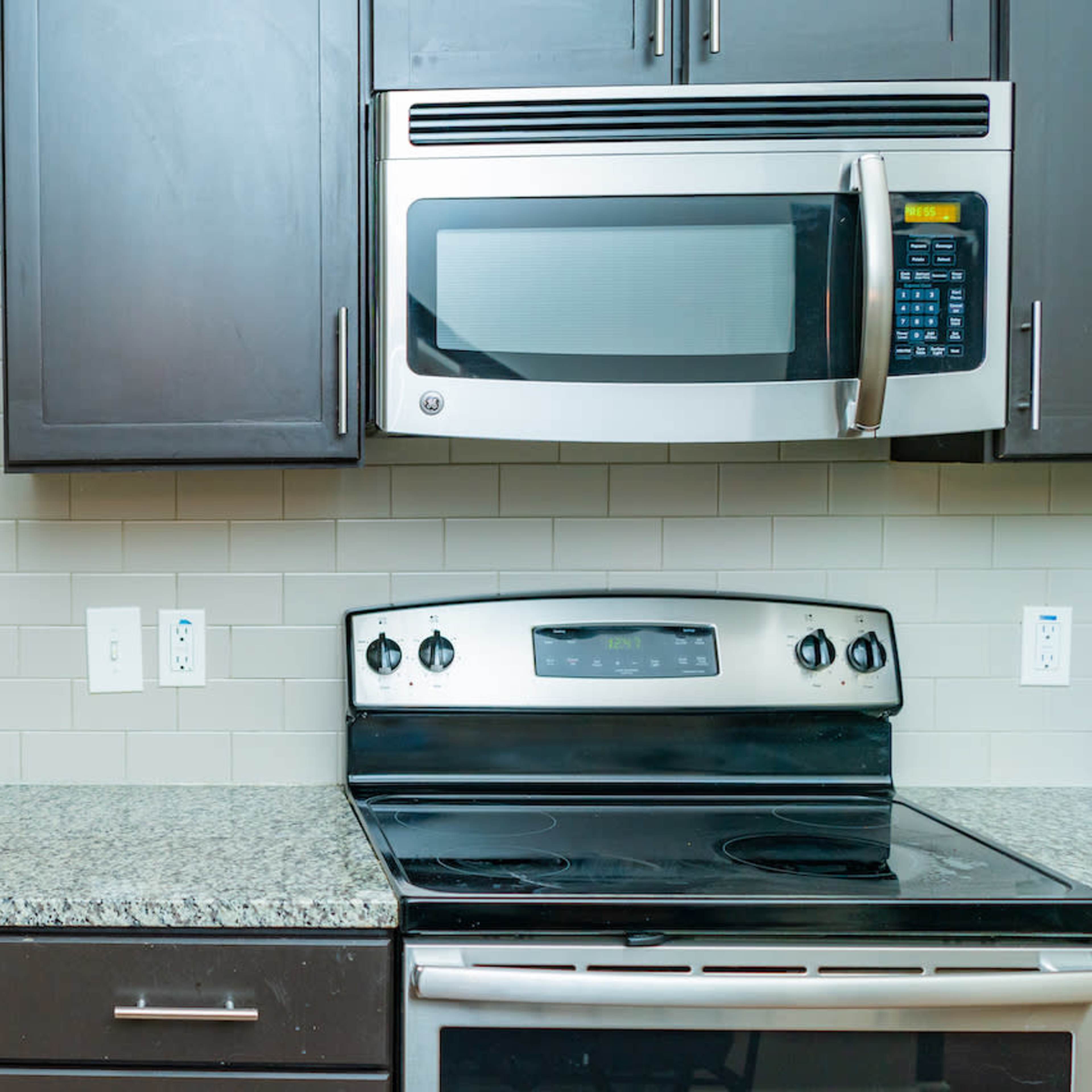 A kitchen with dark cabinets, a stainless steel microwave above a black stove, and a granite countertop with a sink.
