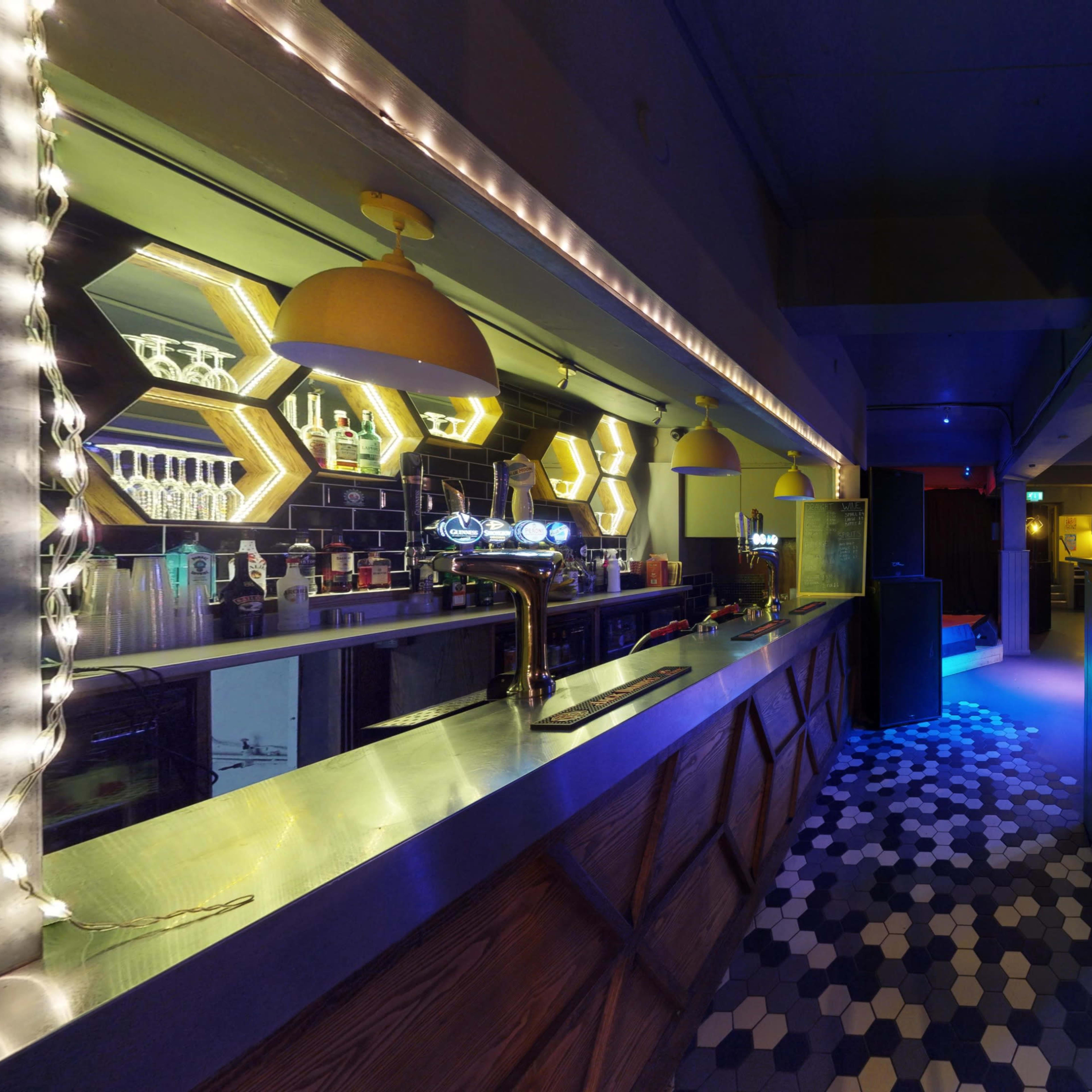 An interior view of a bar with a long counter, colorful lighting, and a patterned floor.