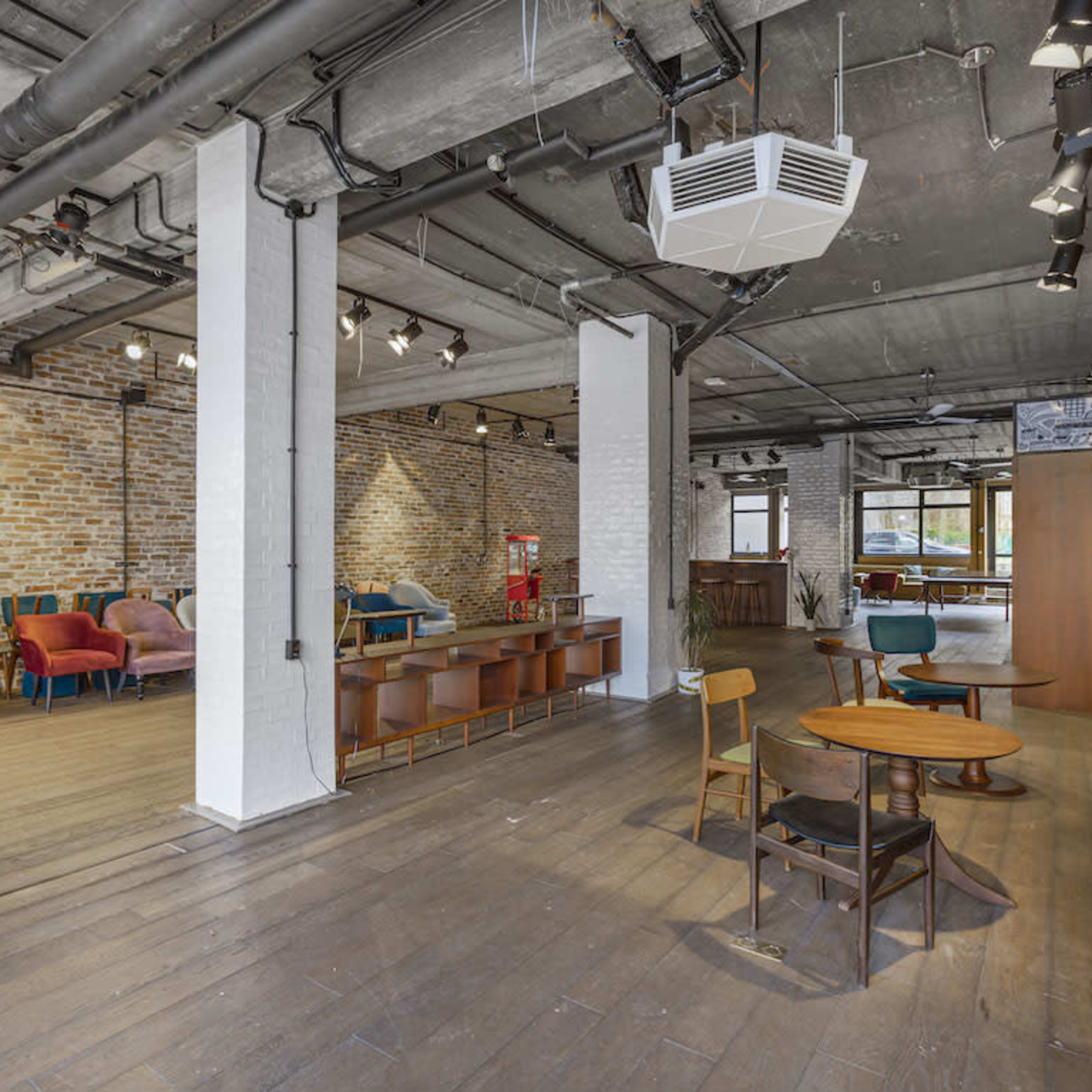 A spacious interior with a mix of seating areas, featuring brick walls, wooden flooring, and various types of furniture arranged in an open layout.