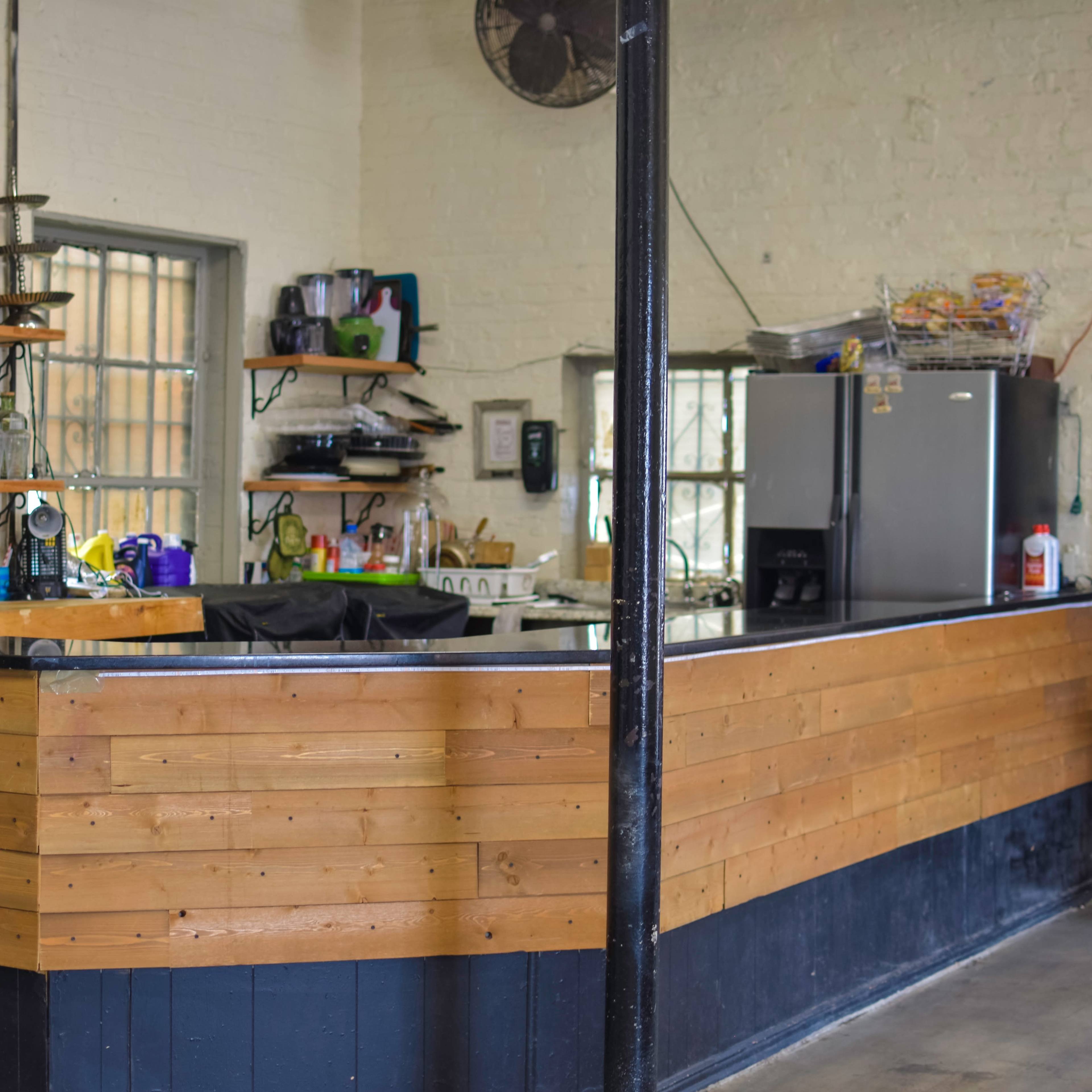 A kitchen bar area with a wooden countertop, shelves displaying various kitchen items, and a refrigerator in the background.