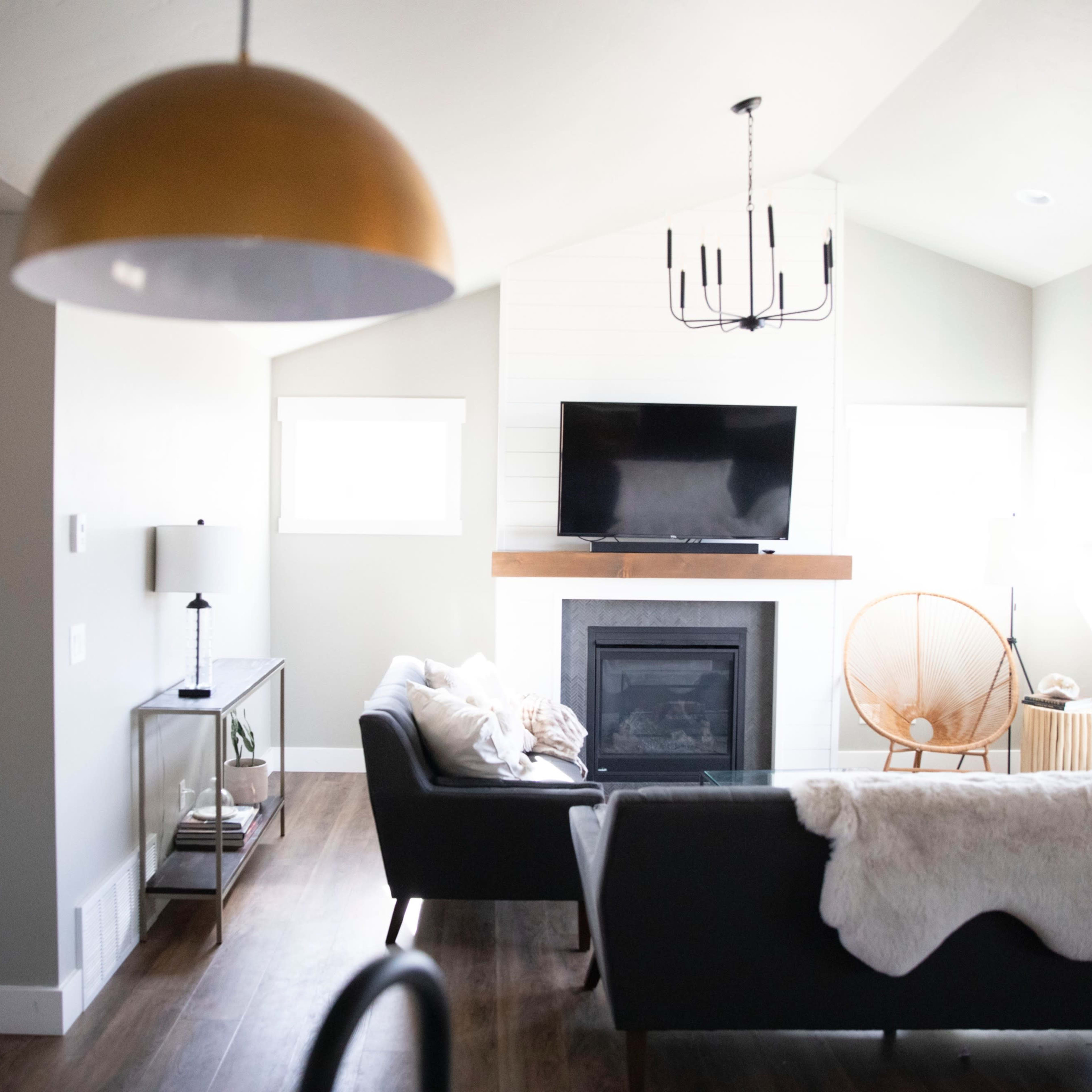 A modern living room featuring a fireplace, a flat-screen TV mounted above the mantel, stylish furniture, and large windows allowing natural light.