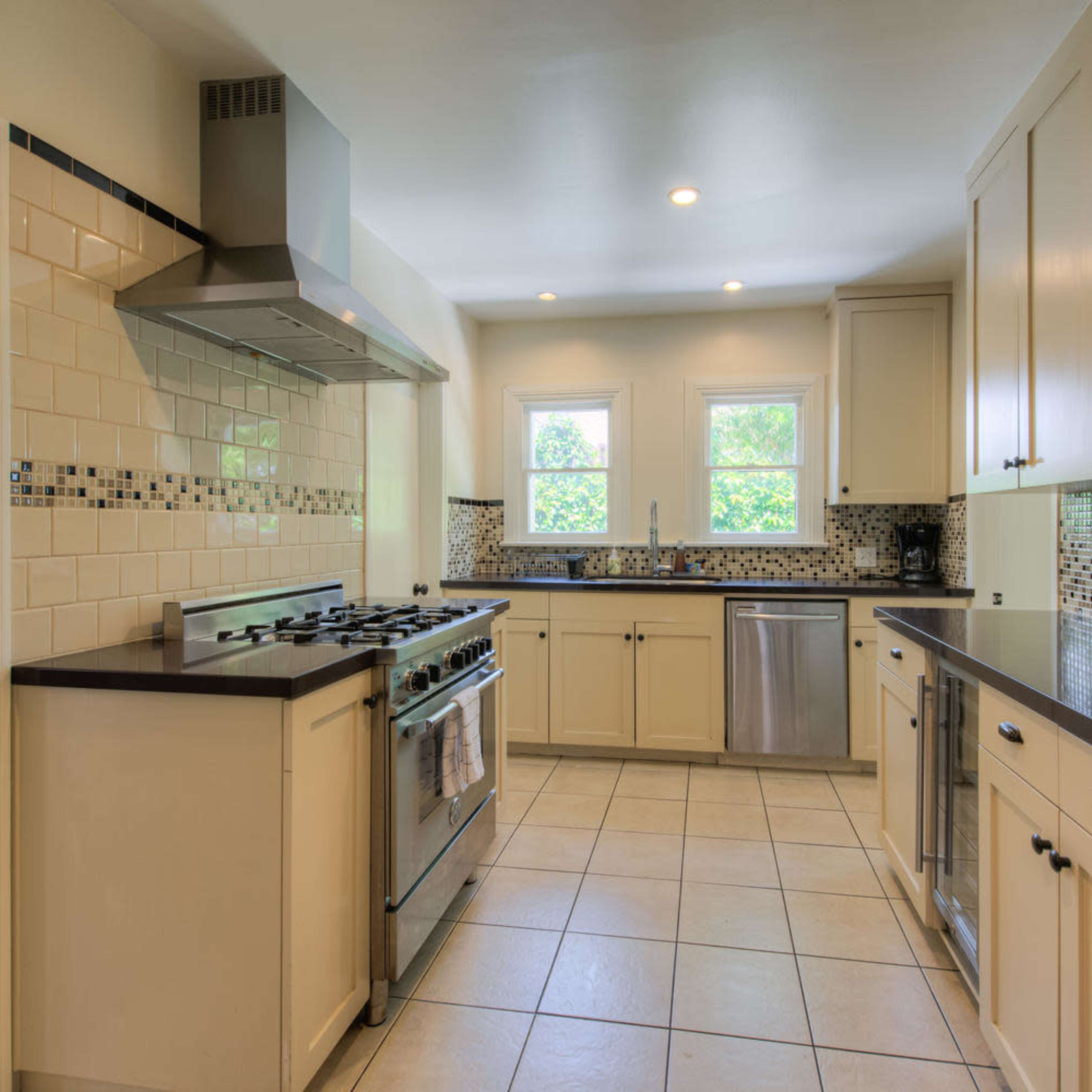 A kitchen features beige cabinets, stainless steel appliances, and tiled flooring with a combination of black and white accents.