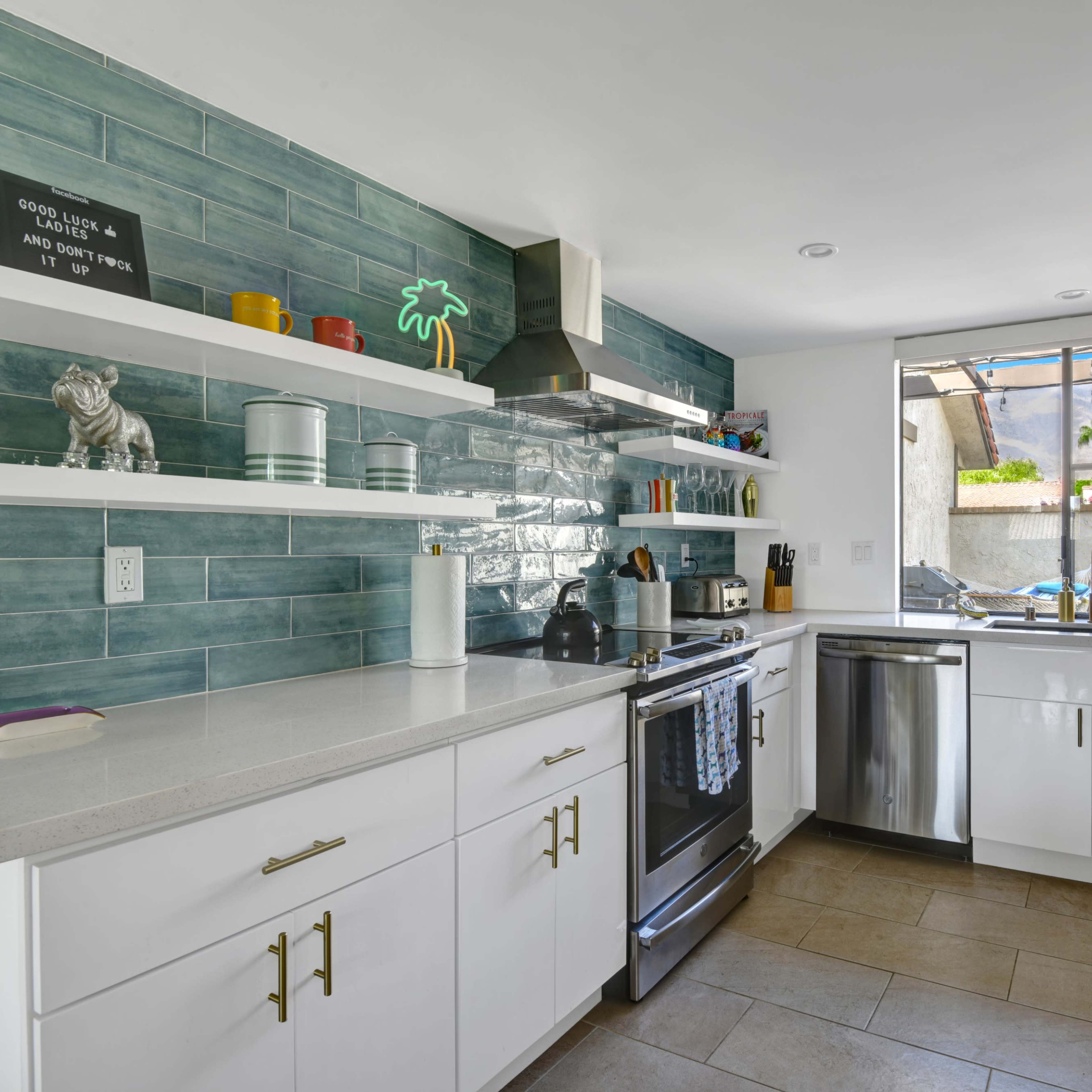 The kitchen features a white cabinet layout with a gray and teal tile backsplash, stainless steel appliances, and a window providing natural light.