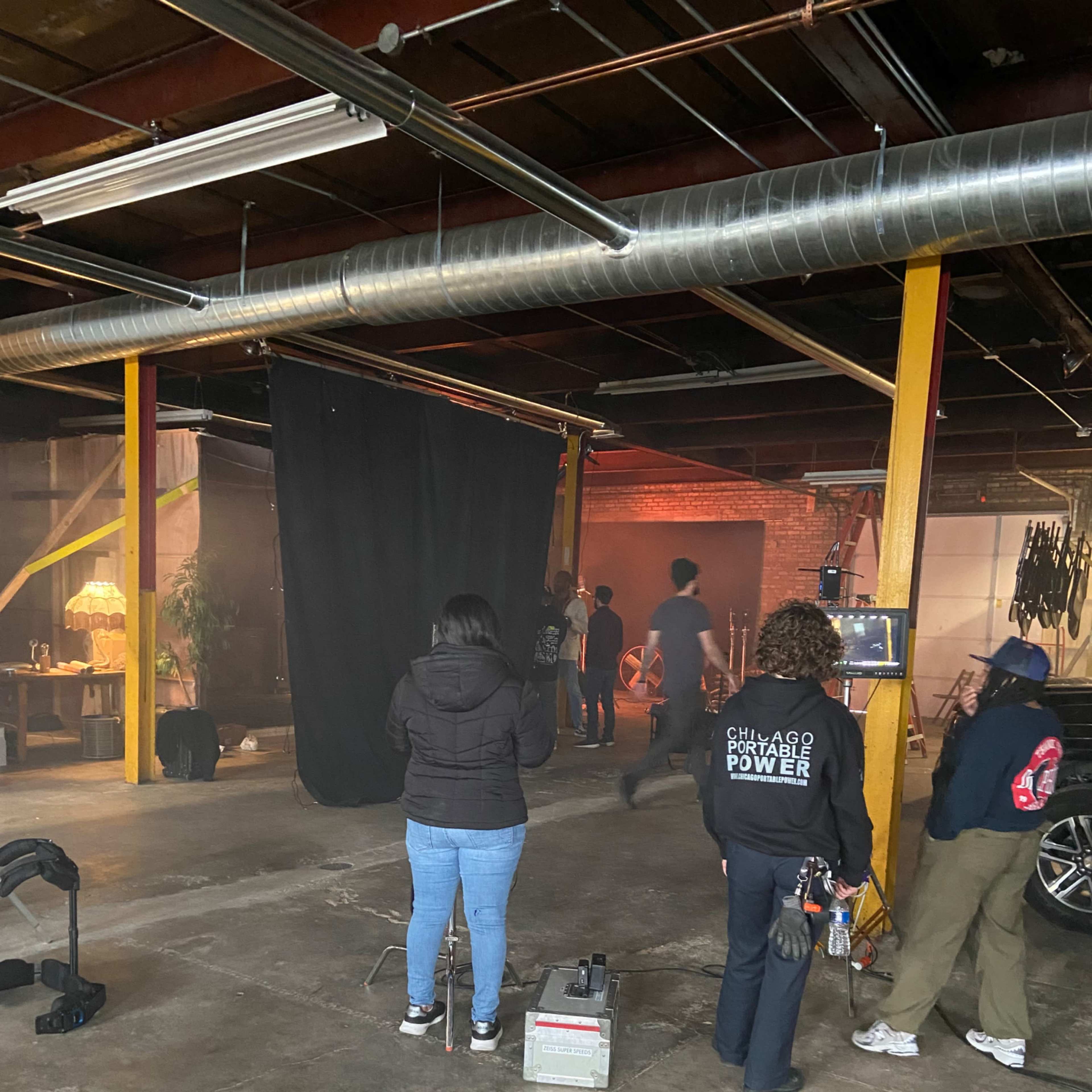 A group of people are working in a dimly lit studio space with a black backdrop and various equipment set up for a photo or video shoot.