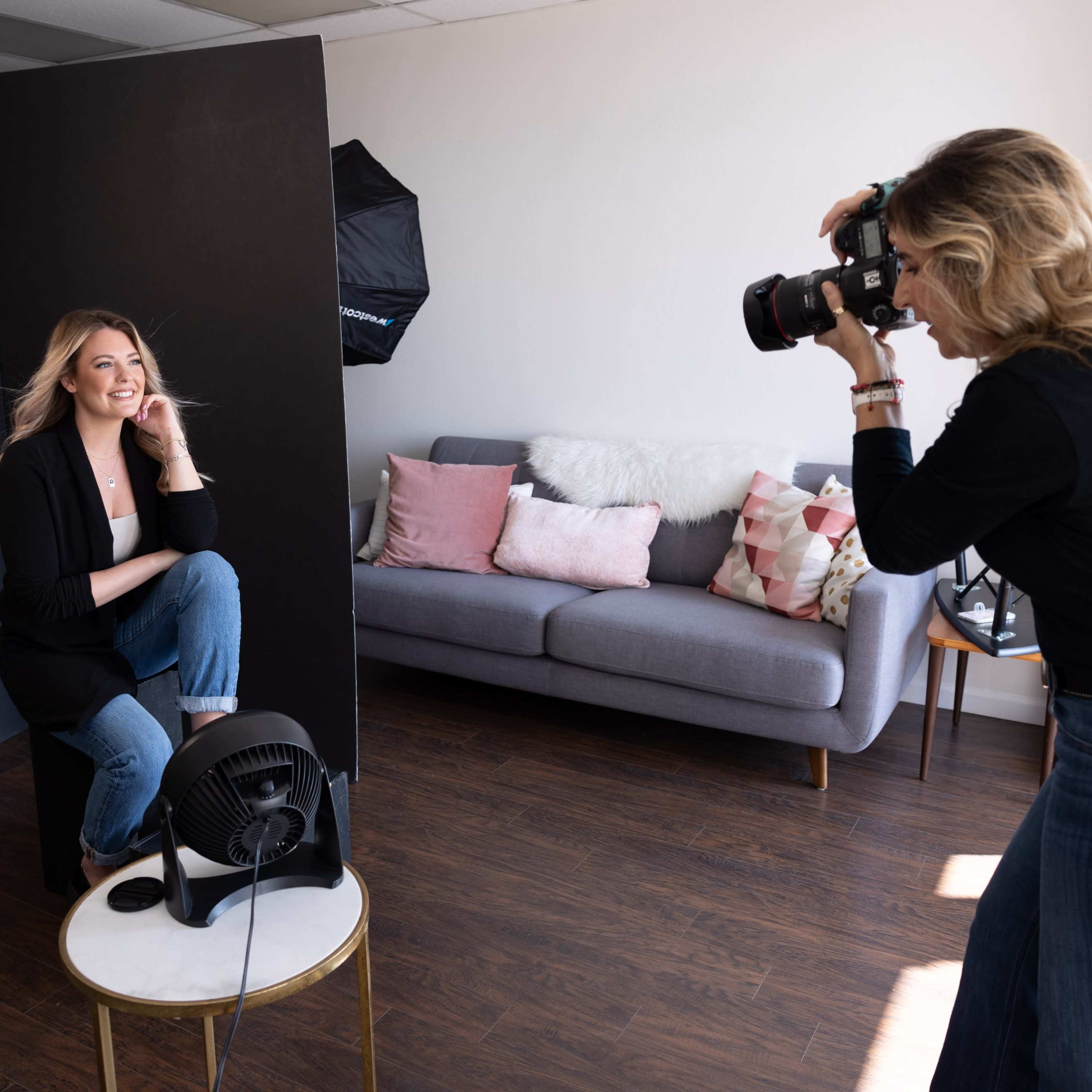 A woman poses for a photo while another woman takes her picture in a well-lit studio setting.