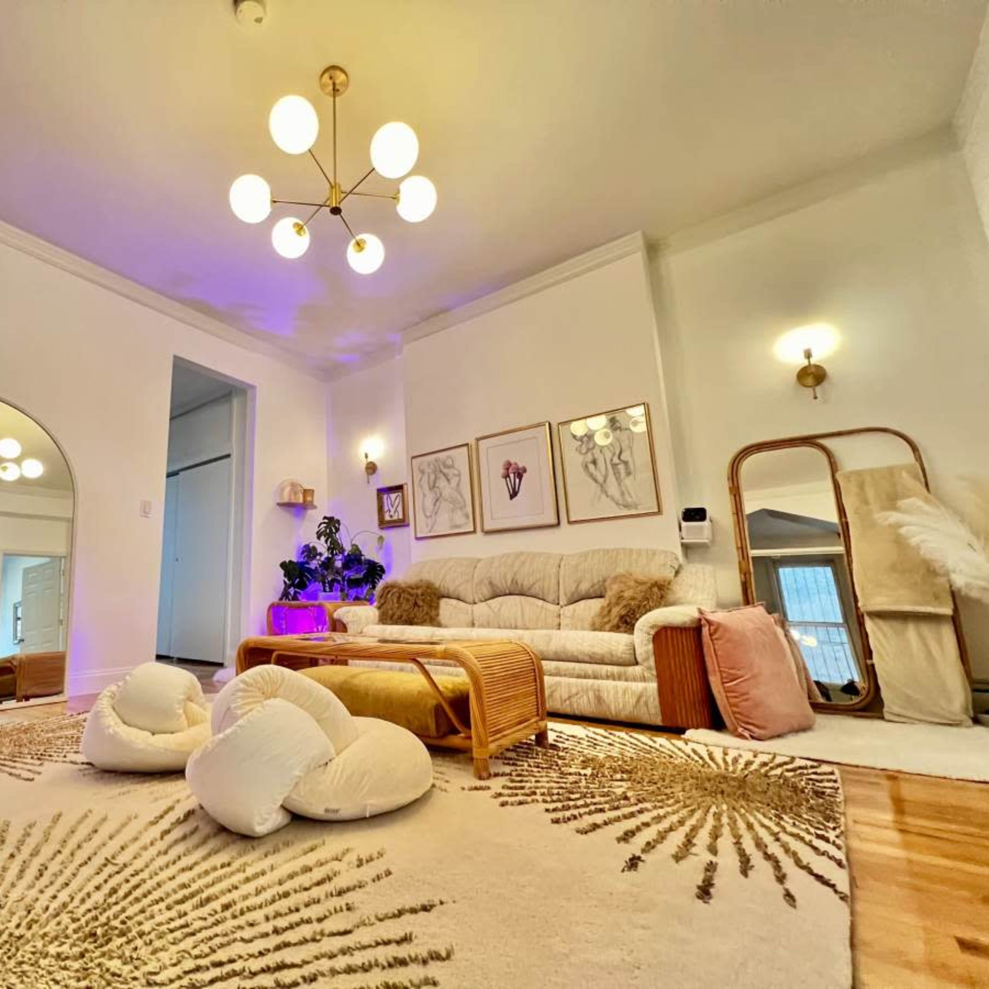 A bright living room featuring a large area rug, plush seating, framed artwork on the walls, and a decorative mirror.